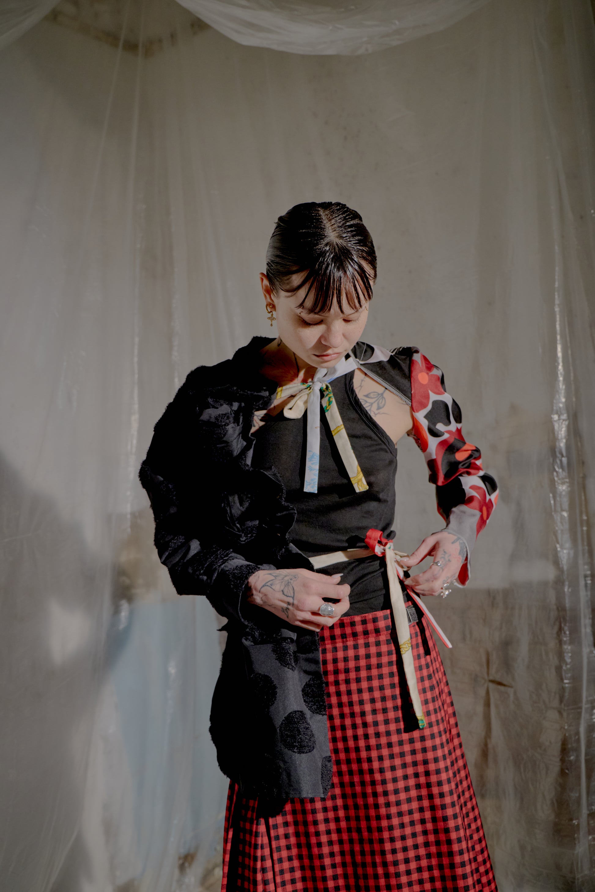 Person wearing a black and red Comme Des Garcons outfit with a checkered skirt, standing against a plain background.