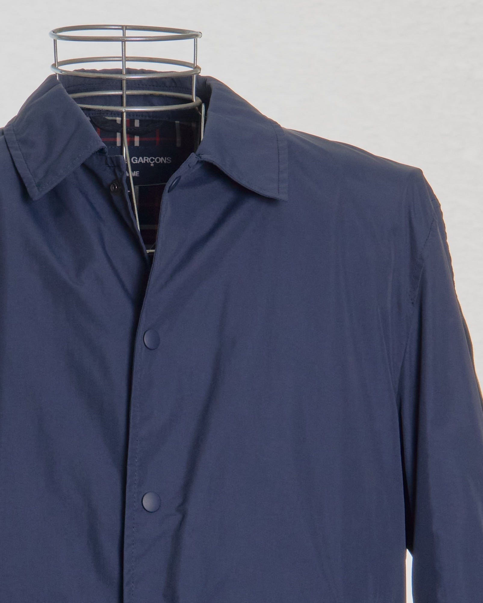 Blue Comme des Garcons coat on a hanger against a white background