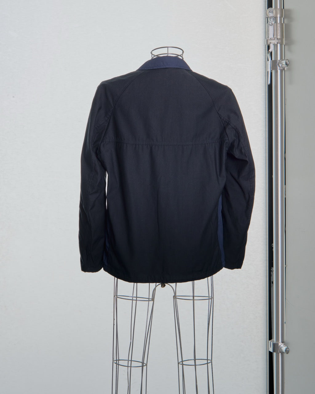 Black and Navy Comme des Garcons jacket on a mannequin against a light gray background