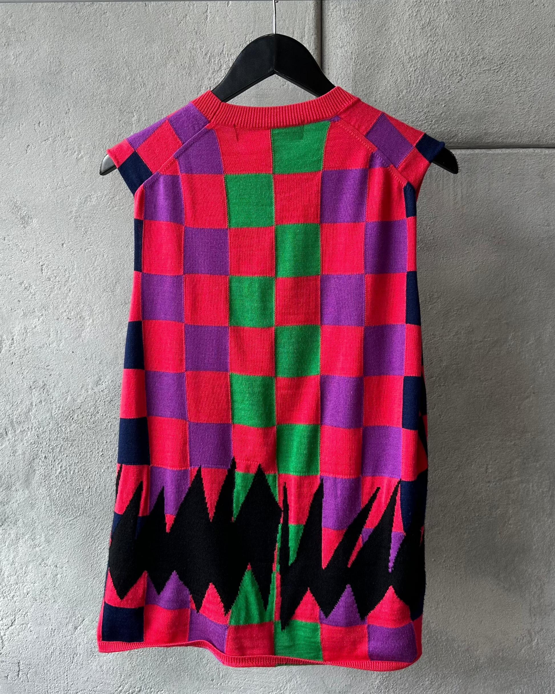 Colourful checkered Comme des Garcons vest on a hanger against a gray wall
