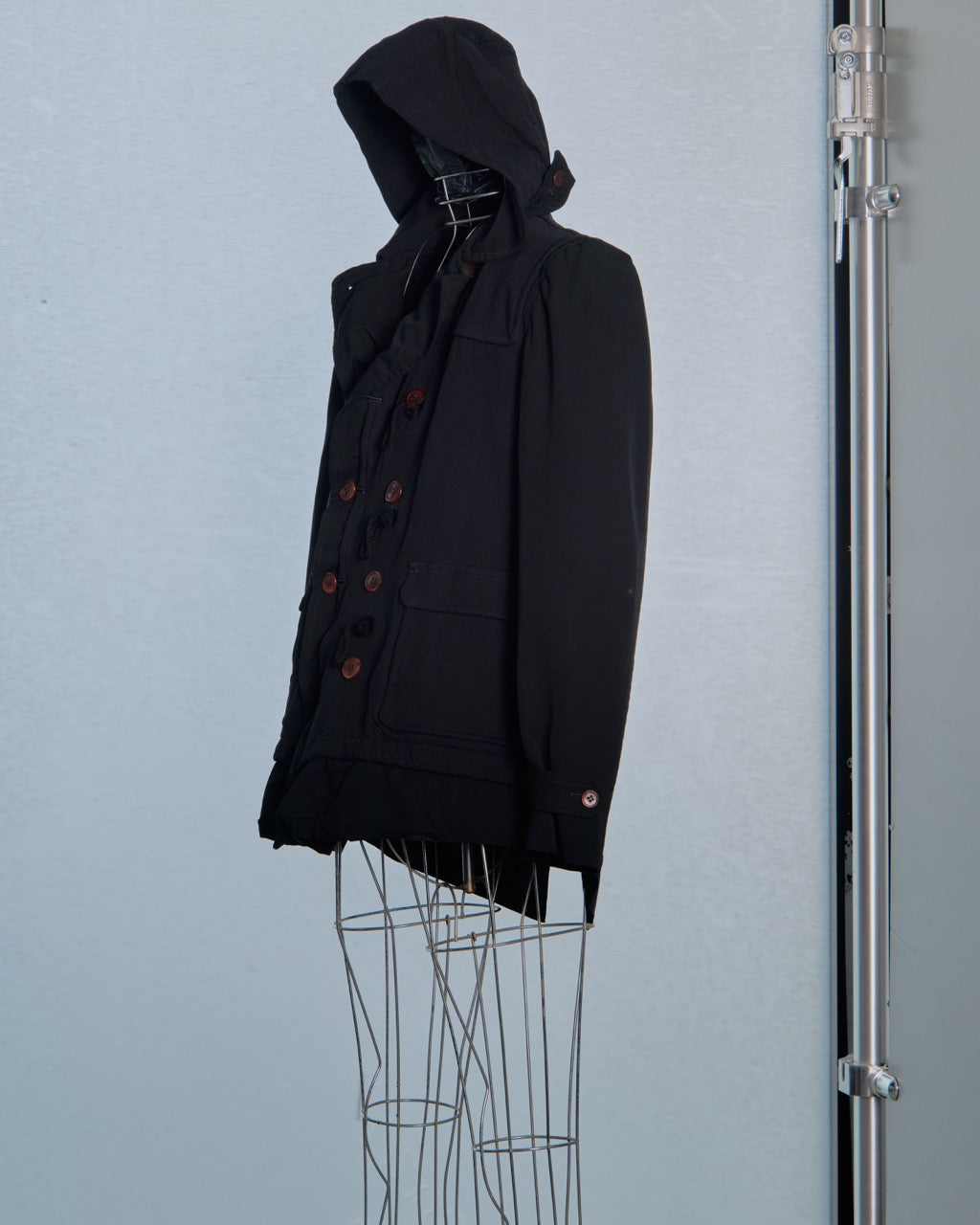 Black hooded Comme des Garcons  jacket on a mannequin against a light blue background