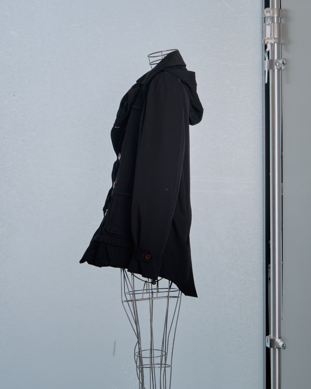 Black Comme des Garcons coat on a mannequin against a light gray background