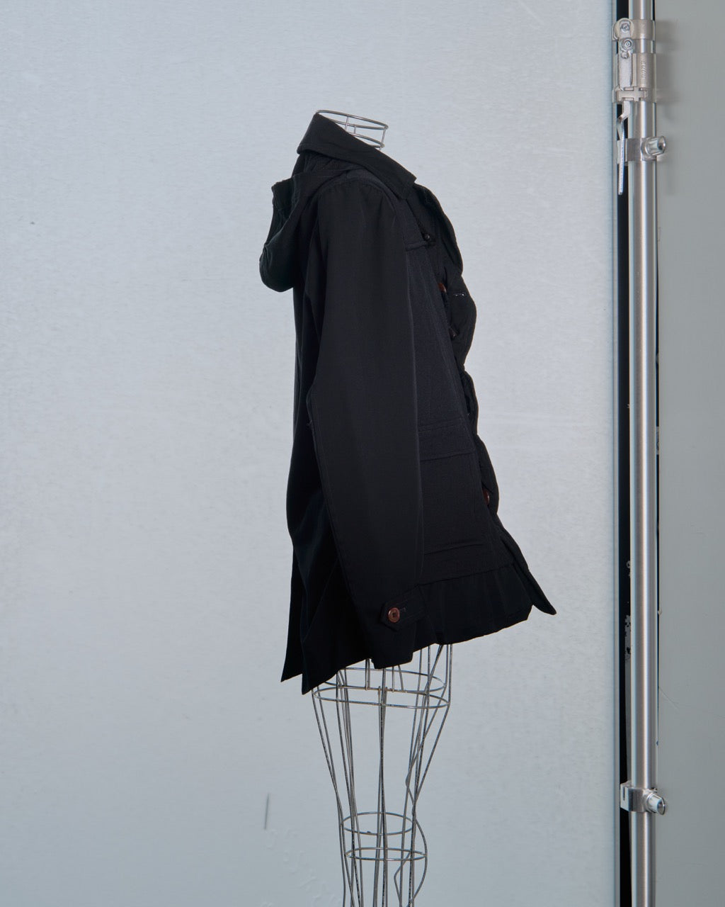 Black Comme des Garcons coat on a mannequin against a plain background