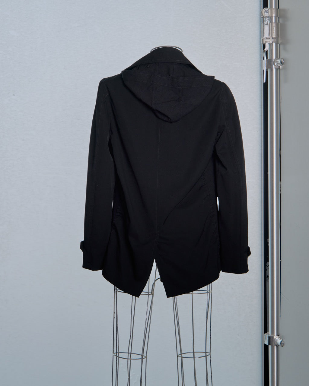 Black Comme des Garcons coat on a mannequin against a gray background