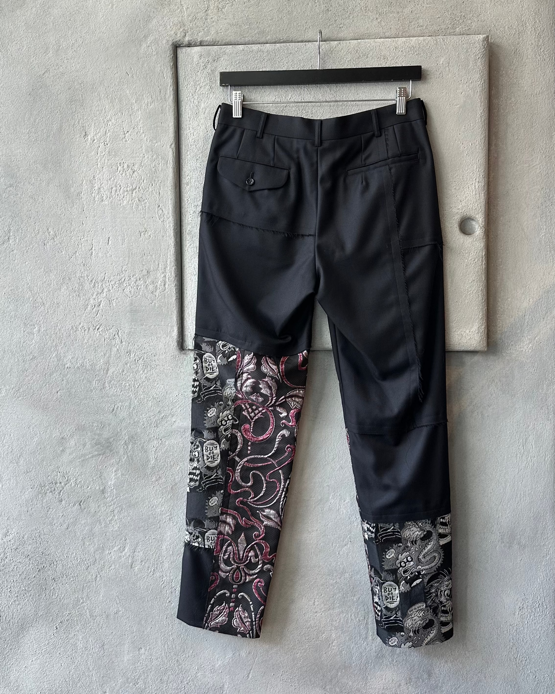 Black Comme des Garcons pants with floral patterns on a concrete wall