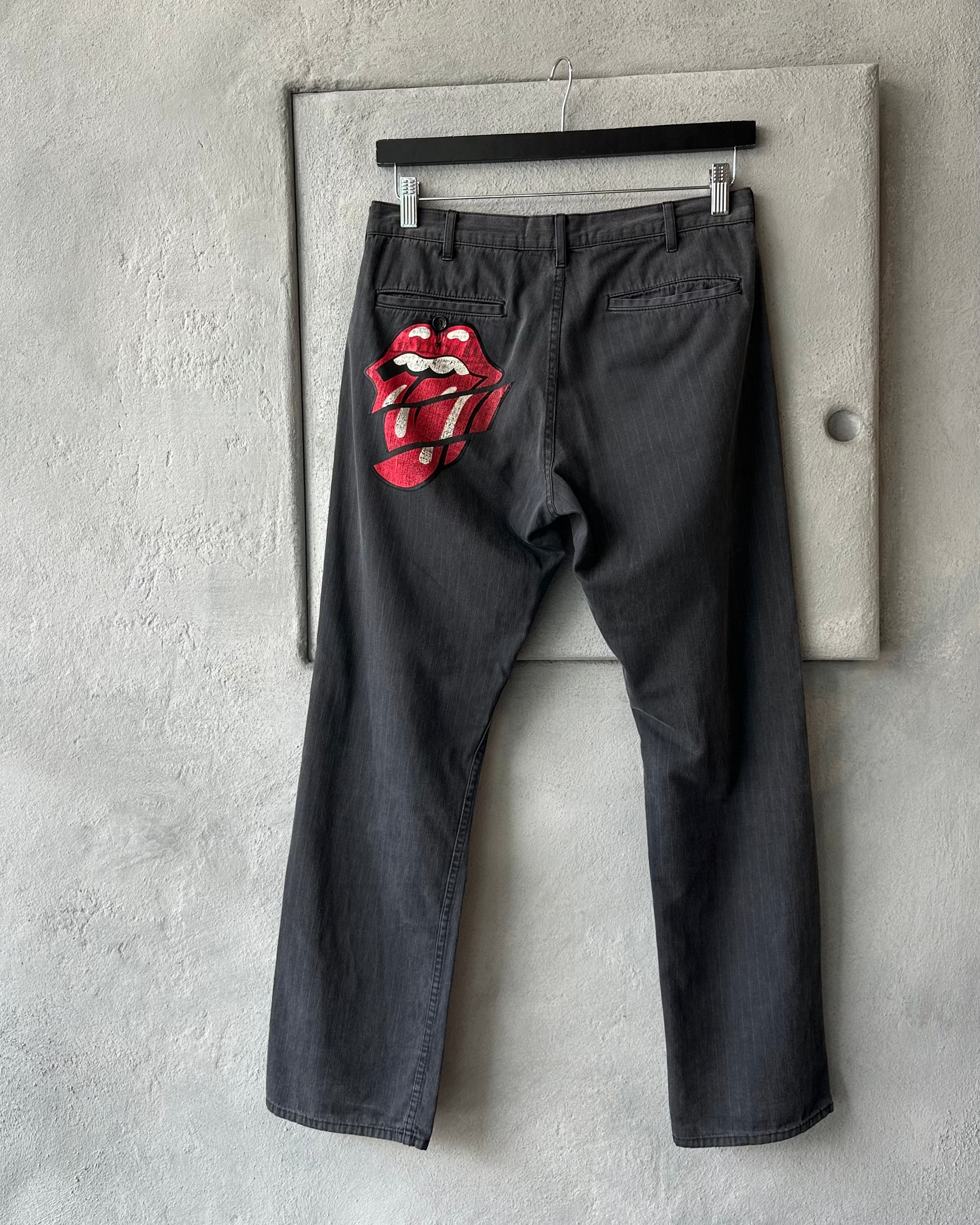 Gray Comme des Garcons pants with Rolling Stones logo on a concrete wall