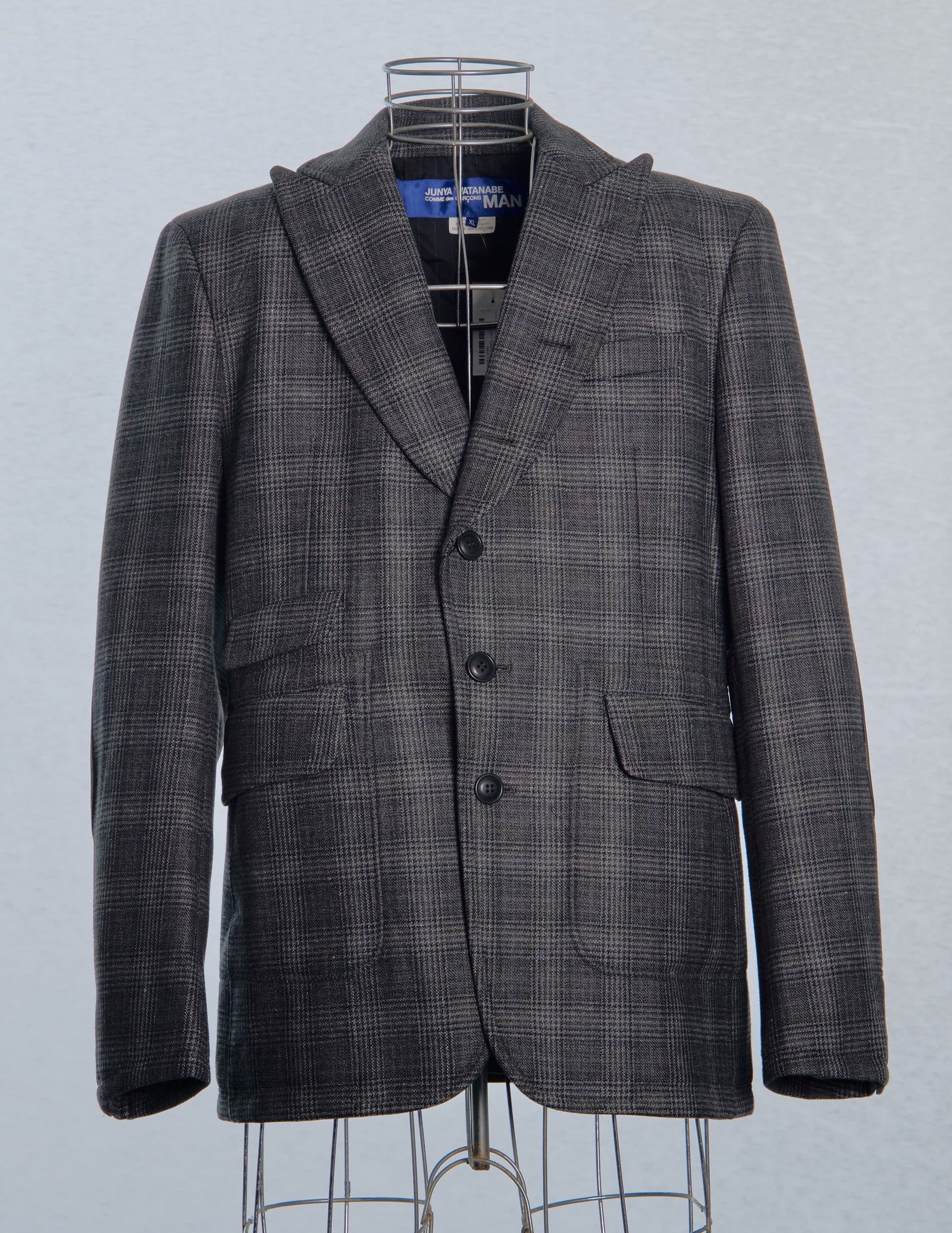 Gray checkered Comme des Garçons Junya Watanabe blazer on a mannequin against a light gray background