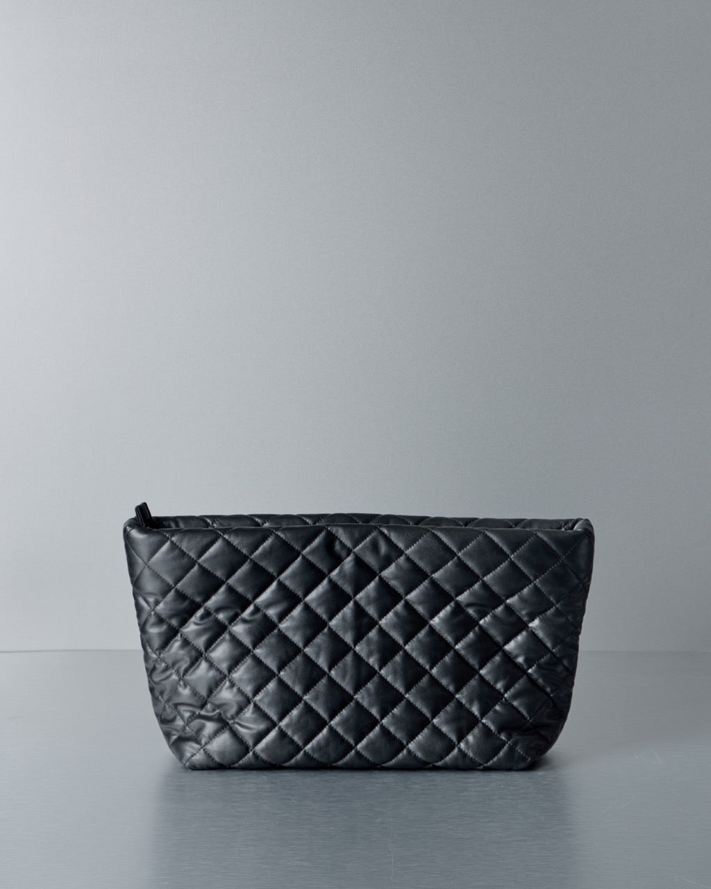 Black quilted Comme des Garcons Junya Watanabe handbag on a gray background