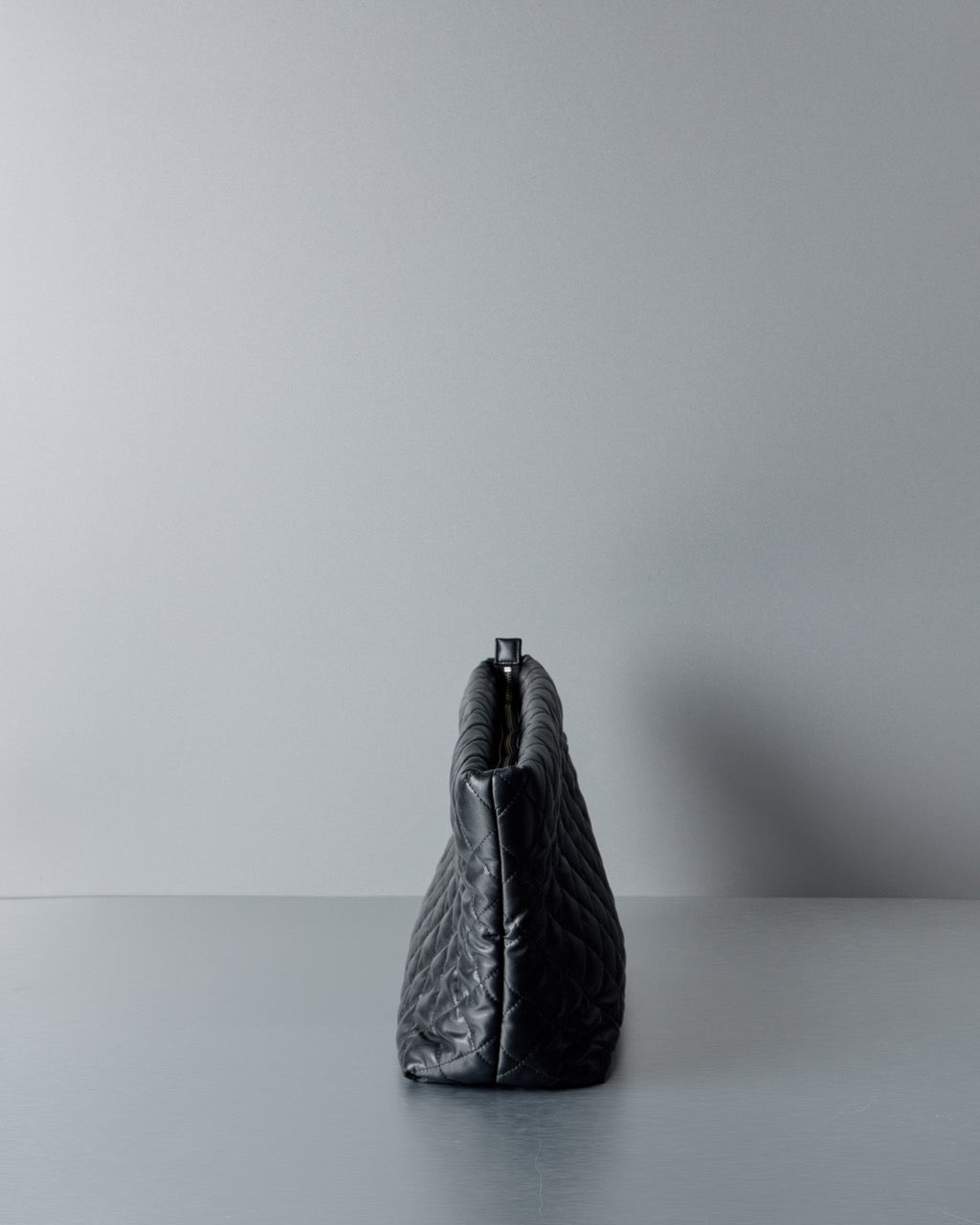 Black quilted Comme des Garcons Junya Watanabe handbag on a gray surface with a light gray background