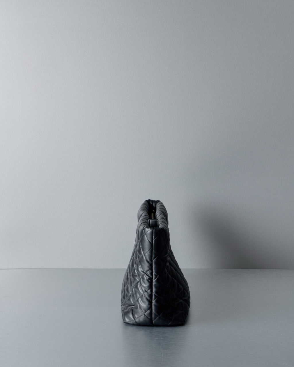 Black quilted Comme des Garcons Junya Watanabe handbag on a light gray surface with a white background