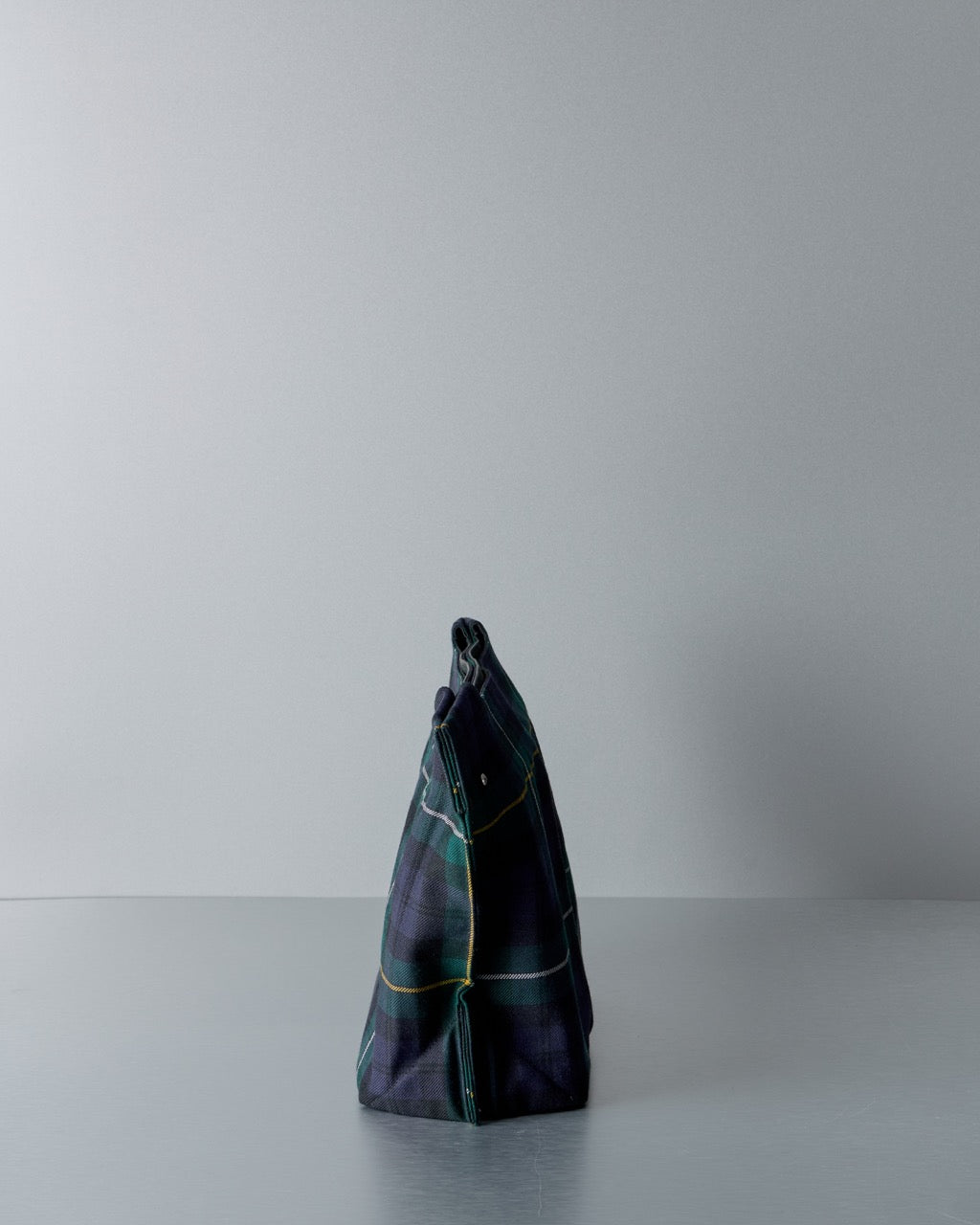 Plaid Comme des Garcons fabric folded into a compact shape on a light gray surface with a white background