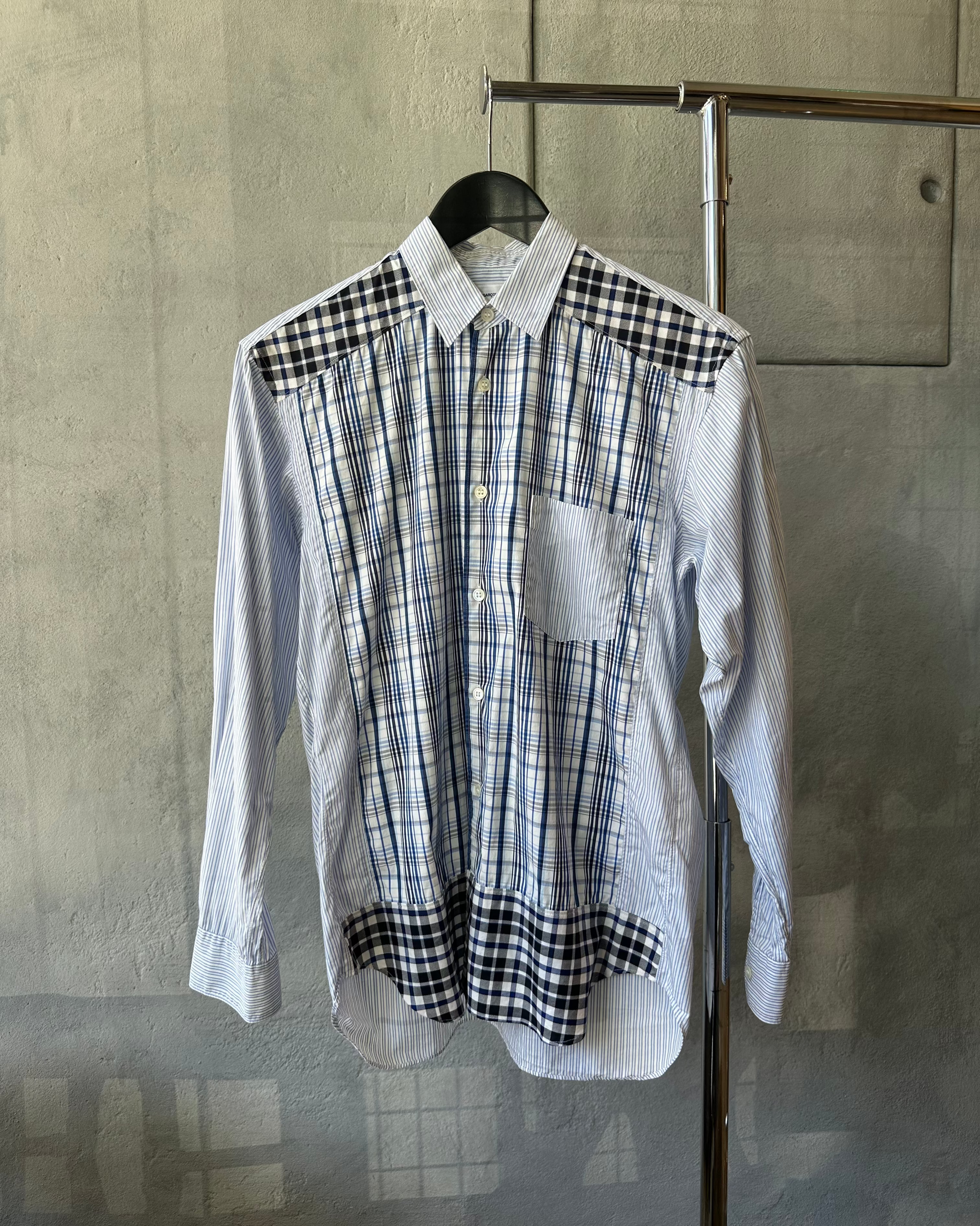 Plaid Comme Des Garcons shirt with black and white pattern on a hanger against a gray wall.