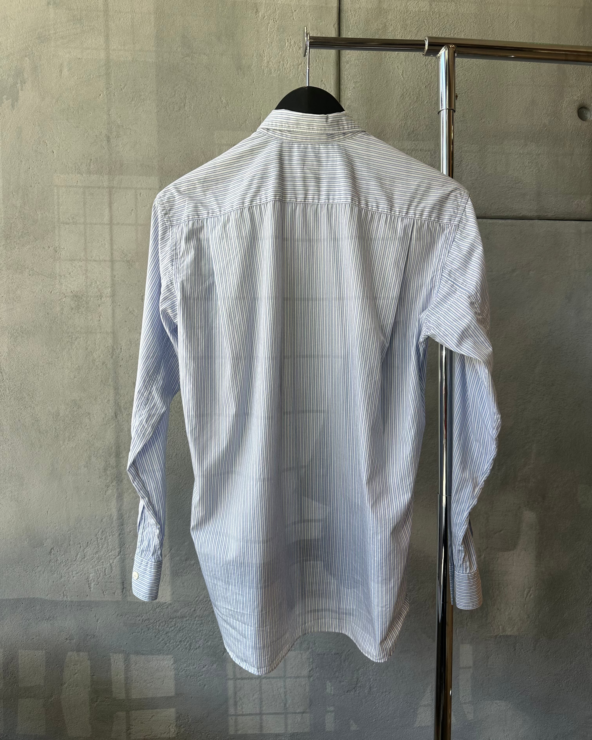 White Comme Des Garcons striped shirt on a hanger against a gray textured wall