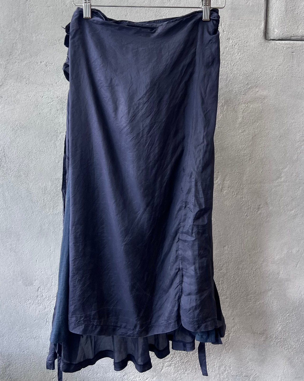 Navy comme des garcons skirt hanging on a rack against a plain wall.