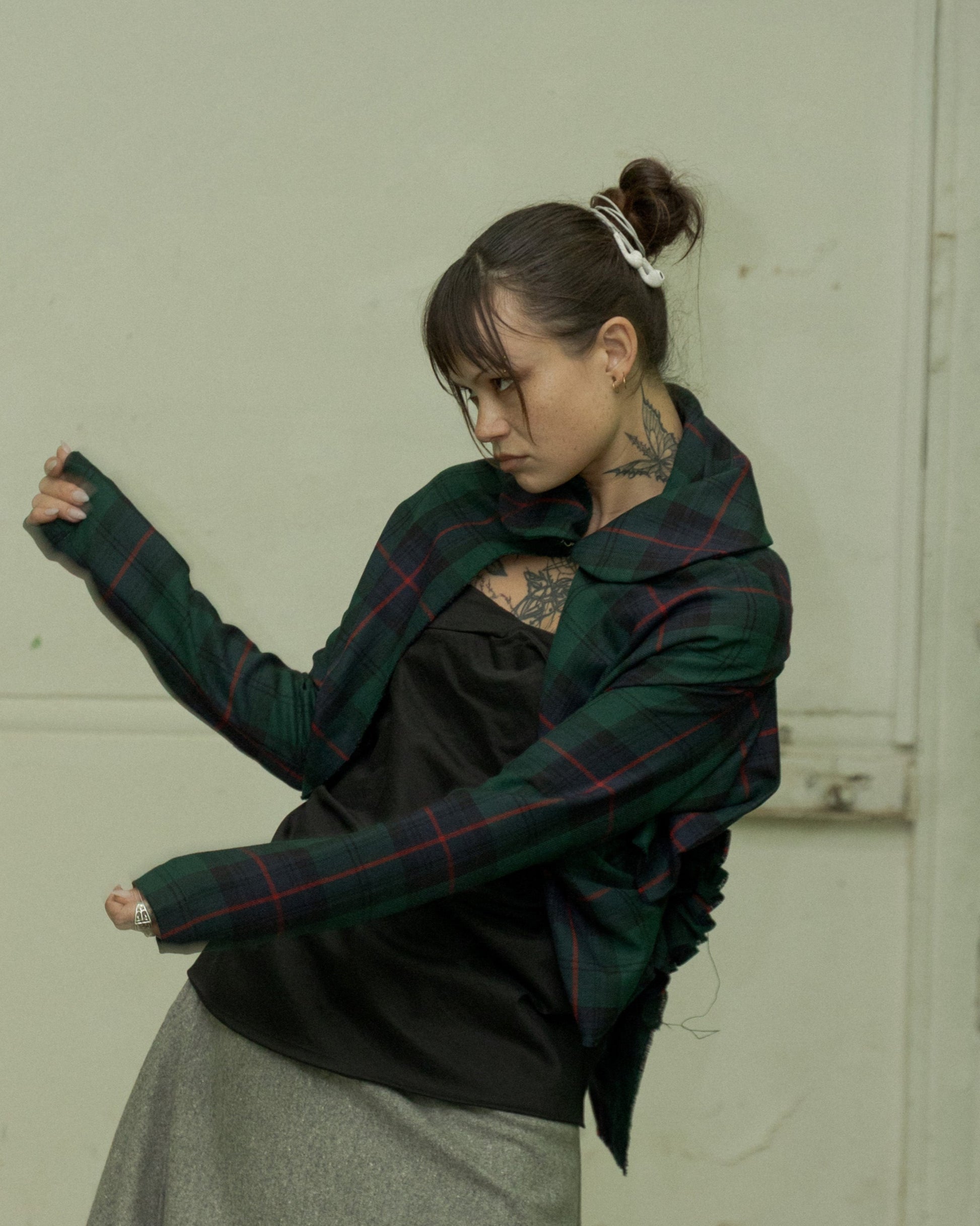 Person wearing a plaid Comme Des Garcons shirt and gray skirt in an abandoned interior setting