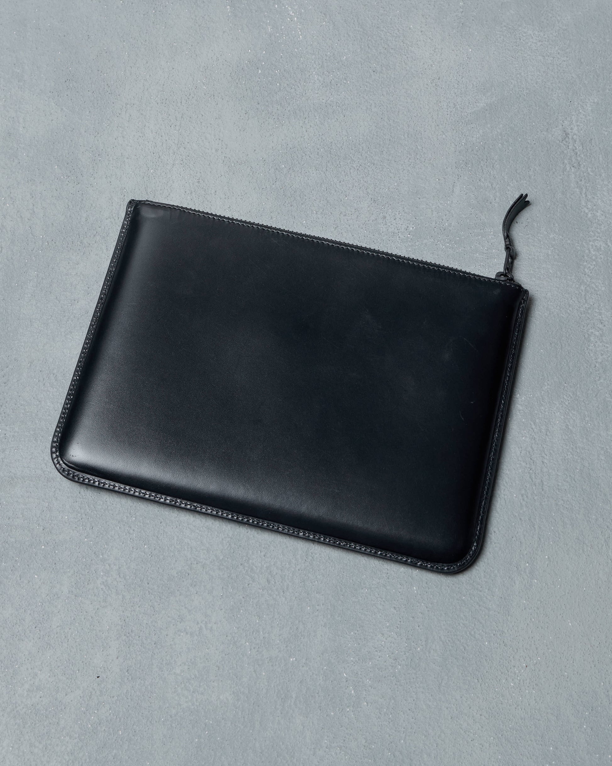 Black leather Comme des Garcons pouch on a gray background