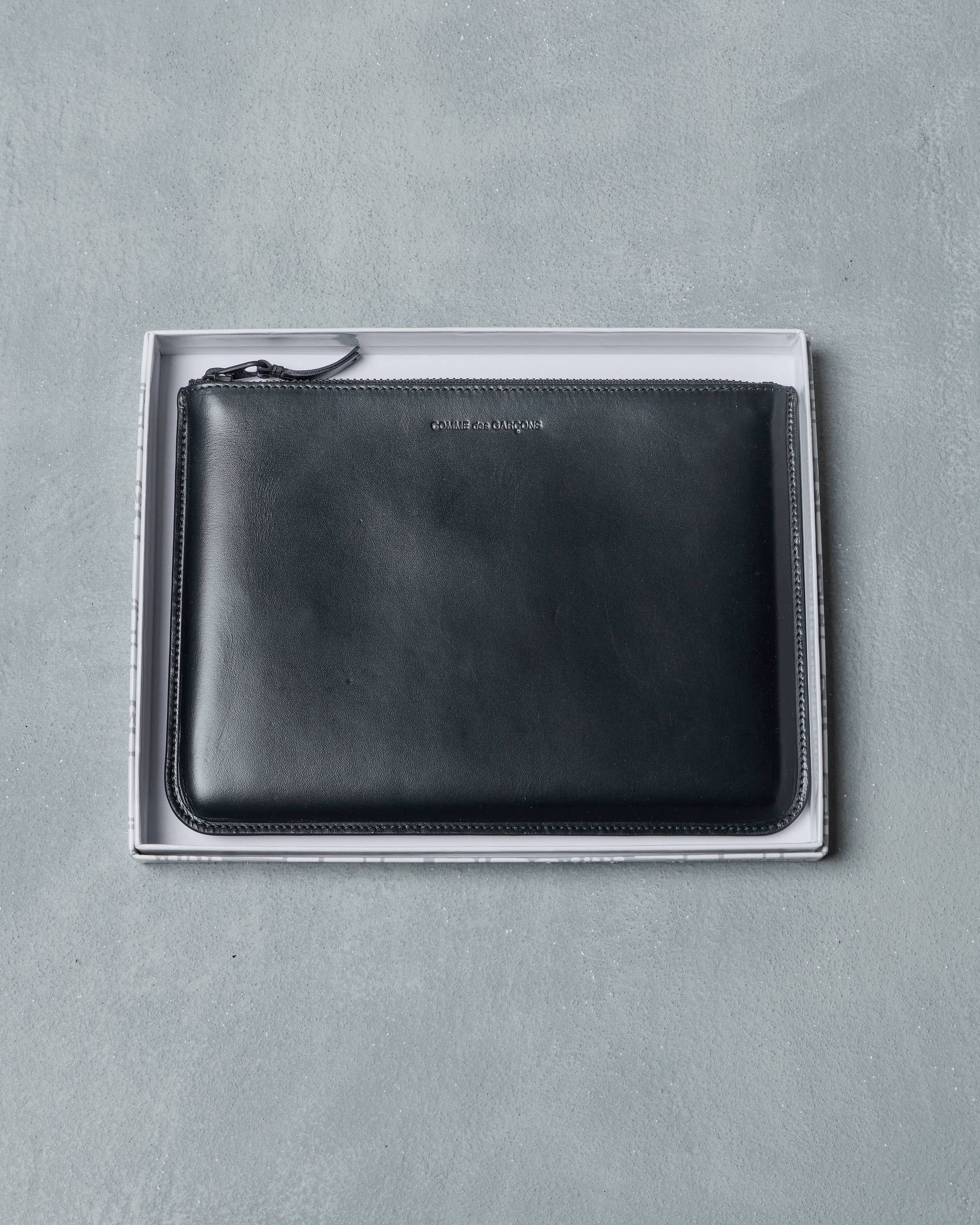 Black leatherComme des Garcons pouch with zipper in original box on a gray background