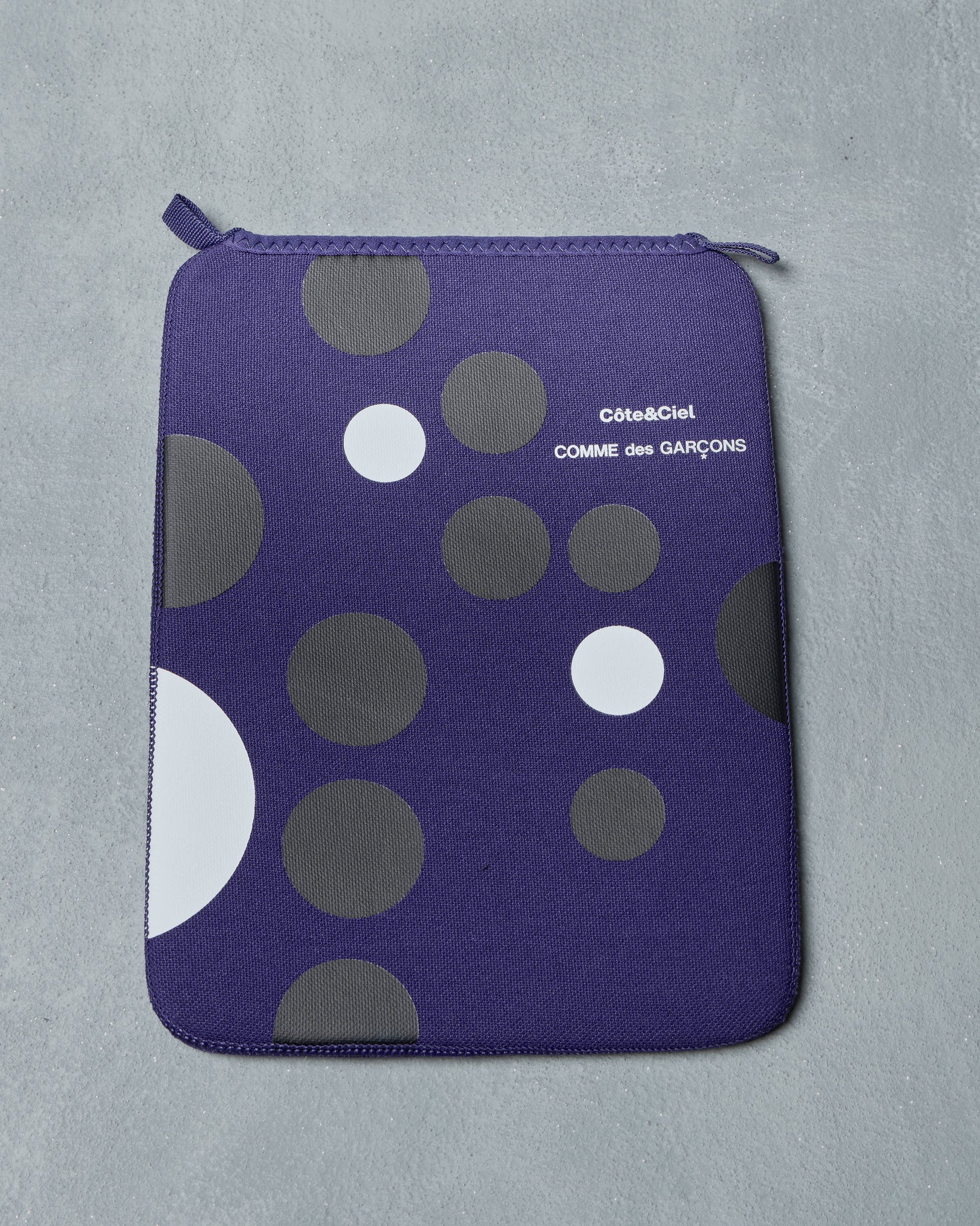 Blue Comme des Garcons ipad pouch with gray and white polka dots on a gray background