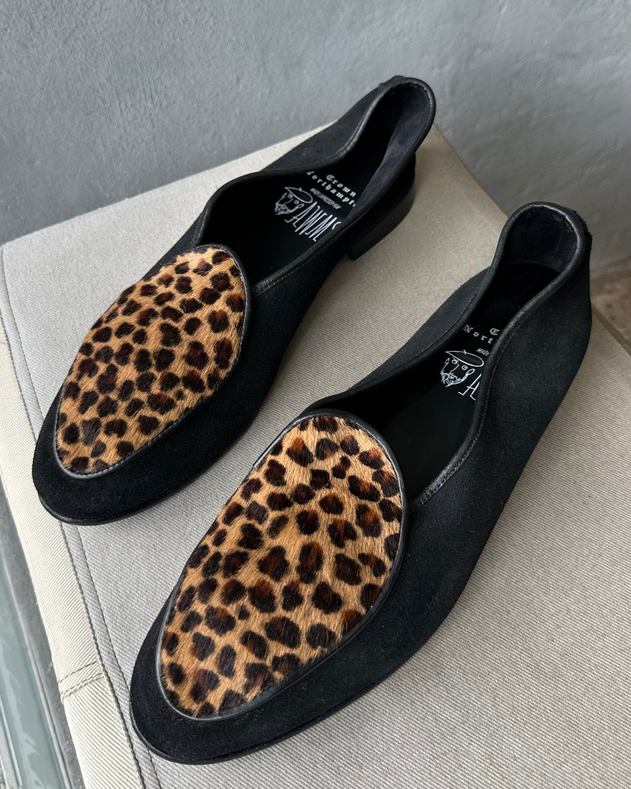 Black Crown Northampton loafers with leopard print soles on a light gray surface