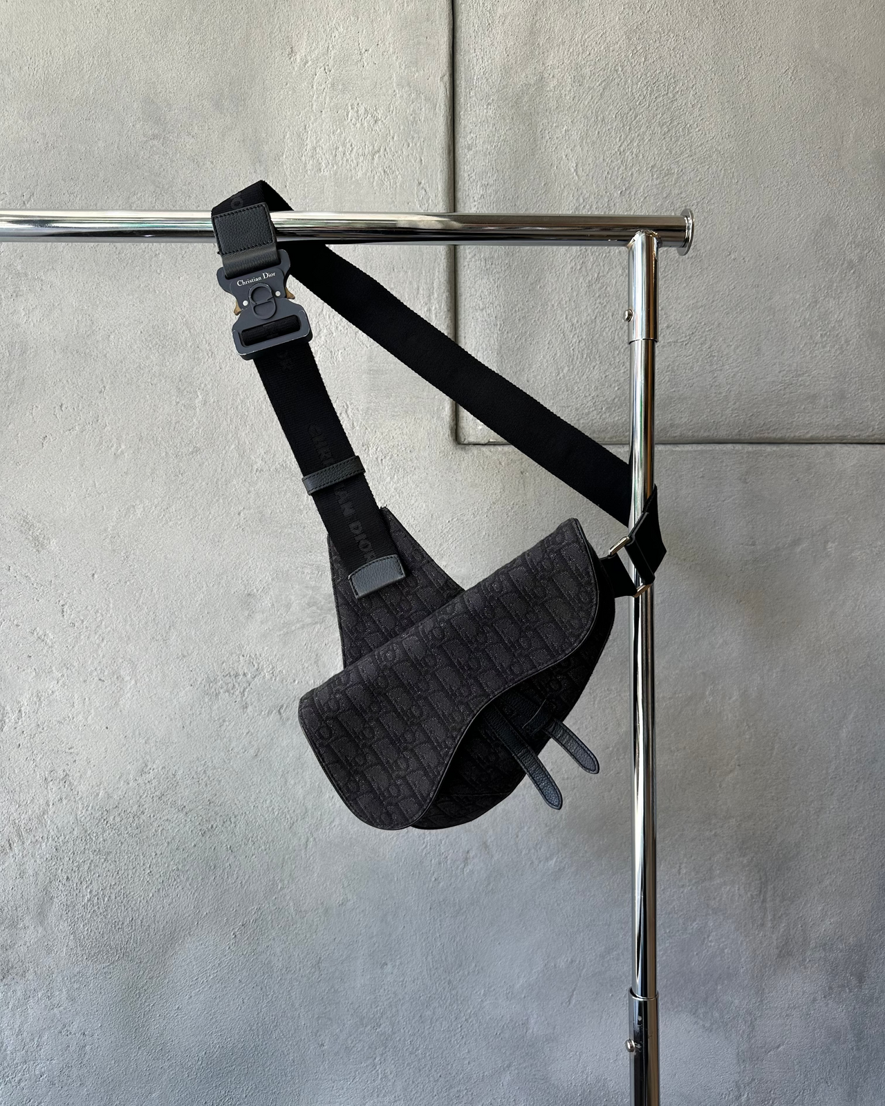 Black Dior harness on a metal stand against a gray tiled wall