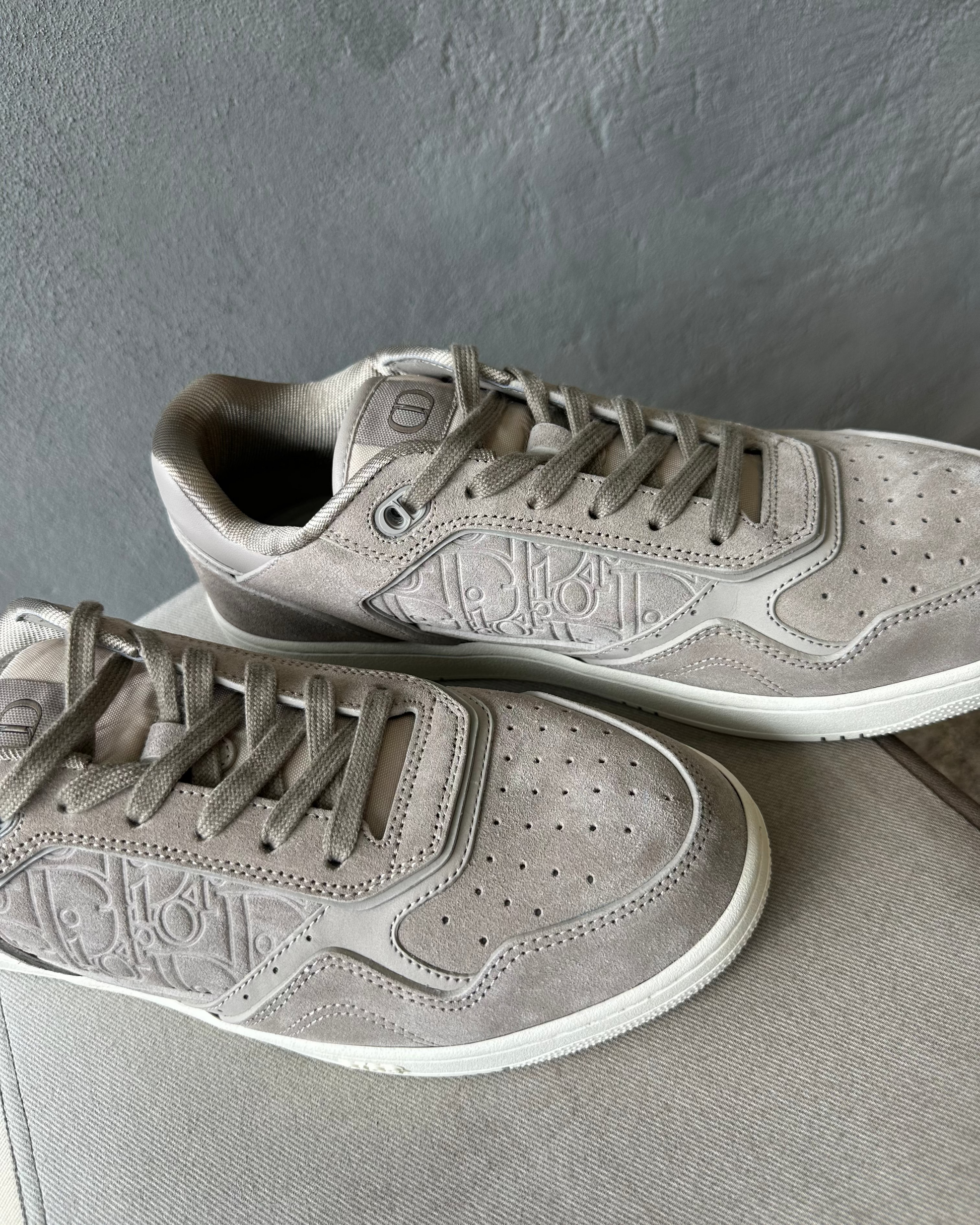 Pair of gray Dior sneakers on a textured surface with a dark gray background