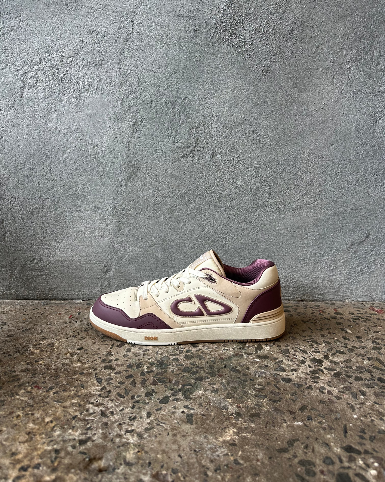 Dior sneaker with purple and white design on a textured surface and gray wall background