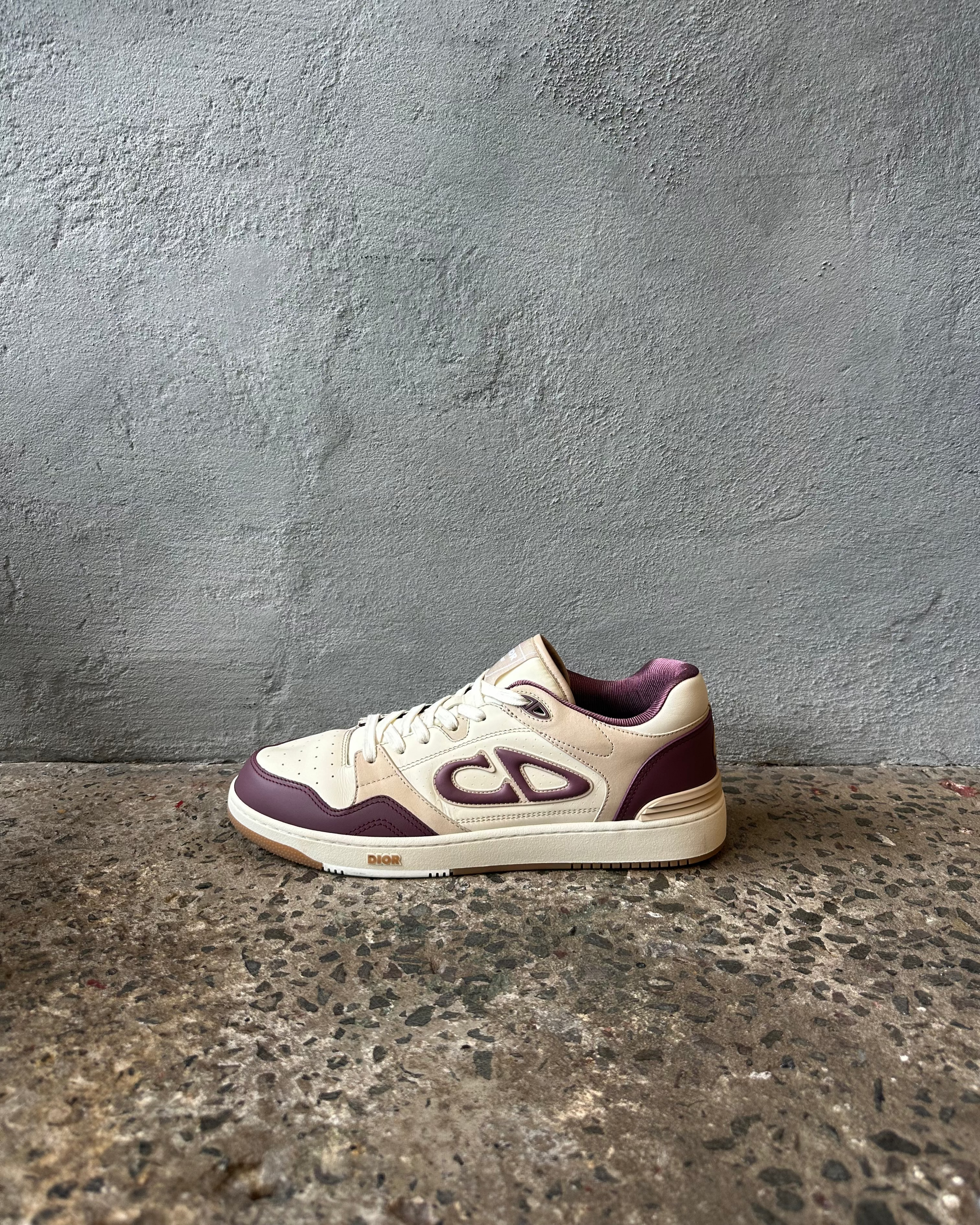 Dior sneaker with purple and white design on a textured surface and gray wall background