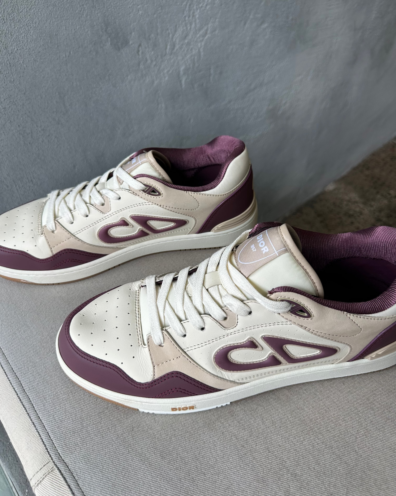 Dior sneaker with purple and white design on a textured surface and gray wall background