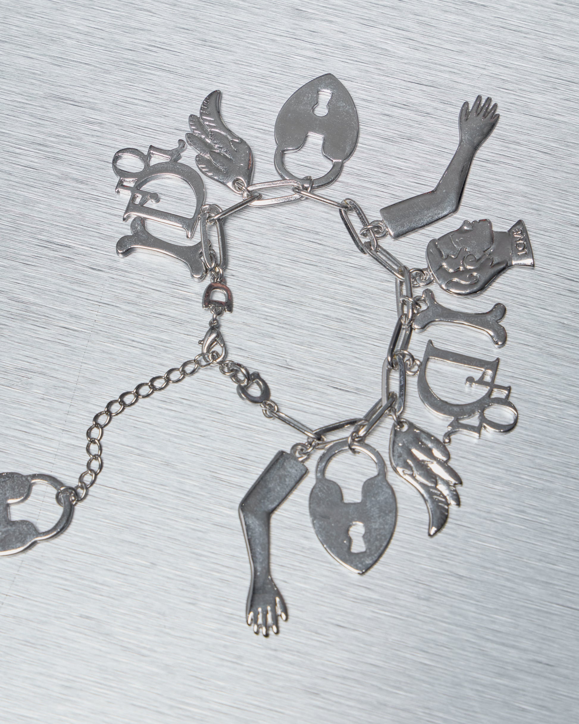 Silver Dior charm bracelet with various charms on a textured gray background