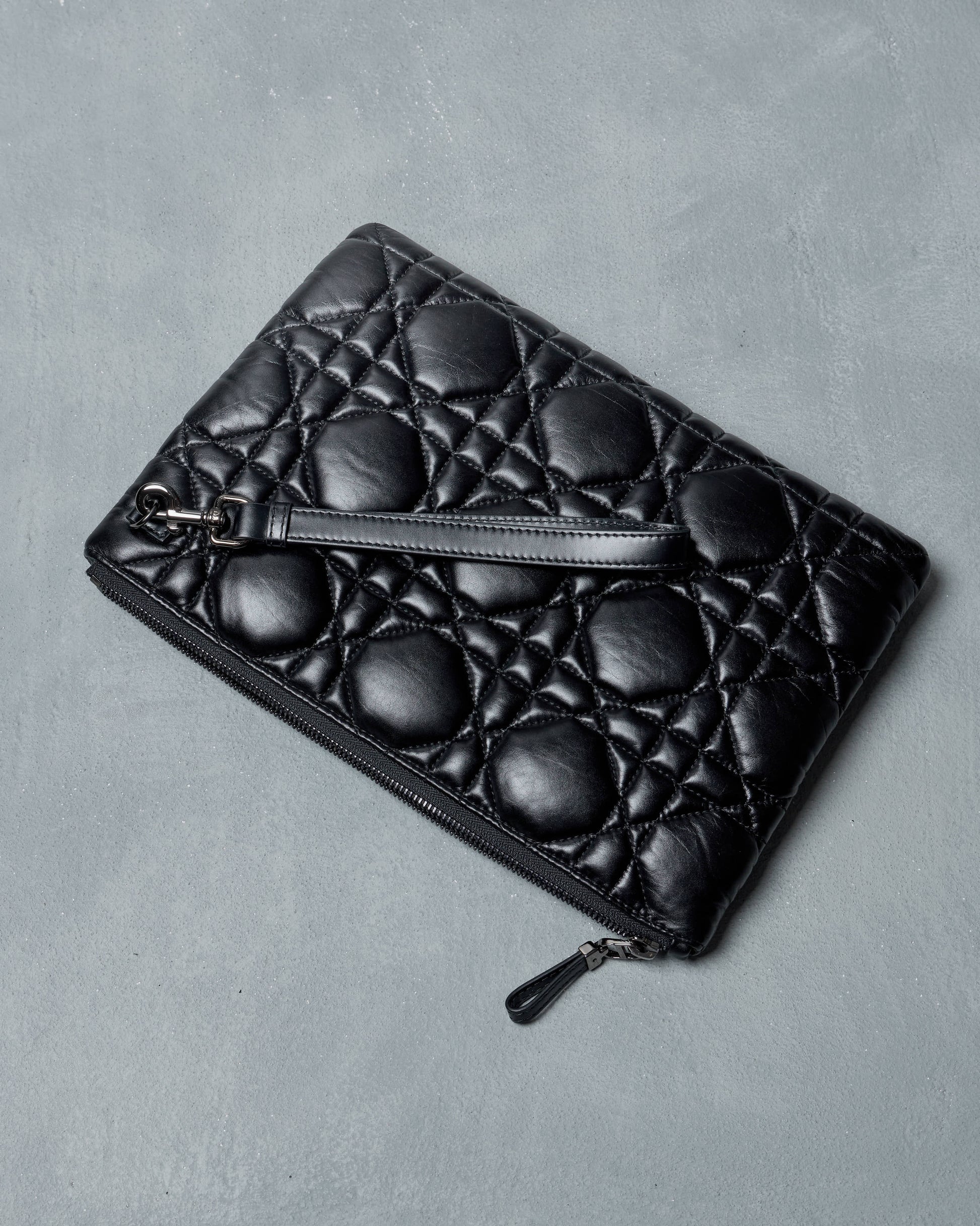 Black quilted Dior clutch bag on a gray background