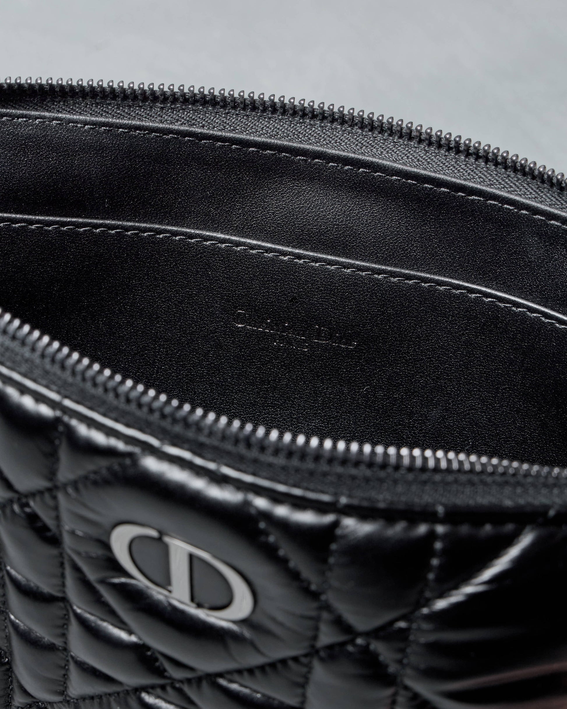 Black quilted Dior bag with a brand logo on a gray background