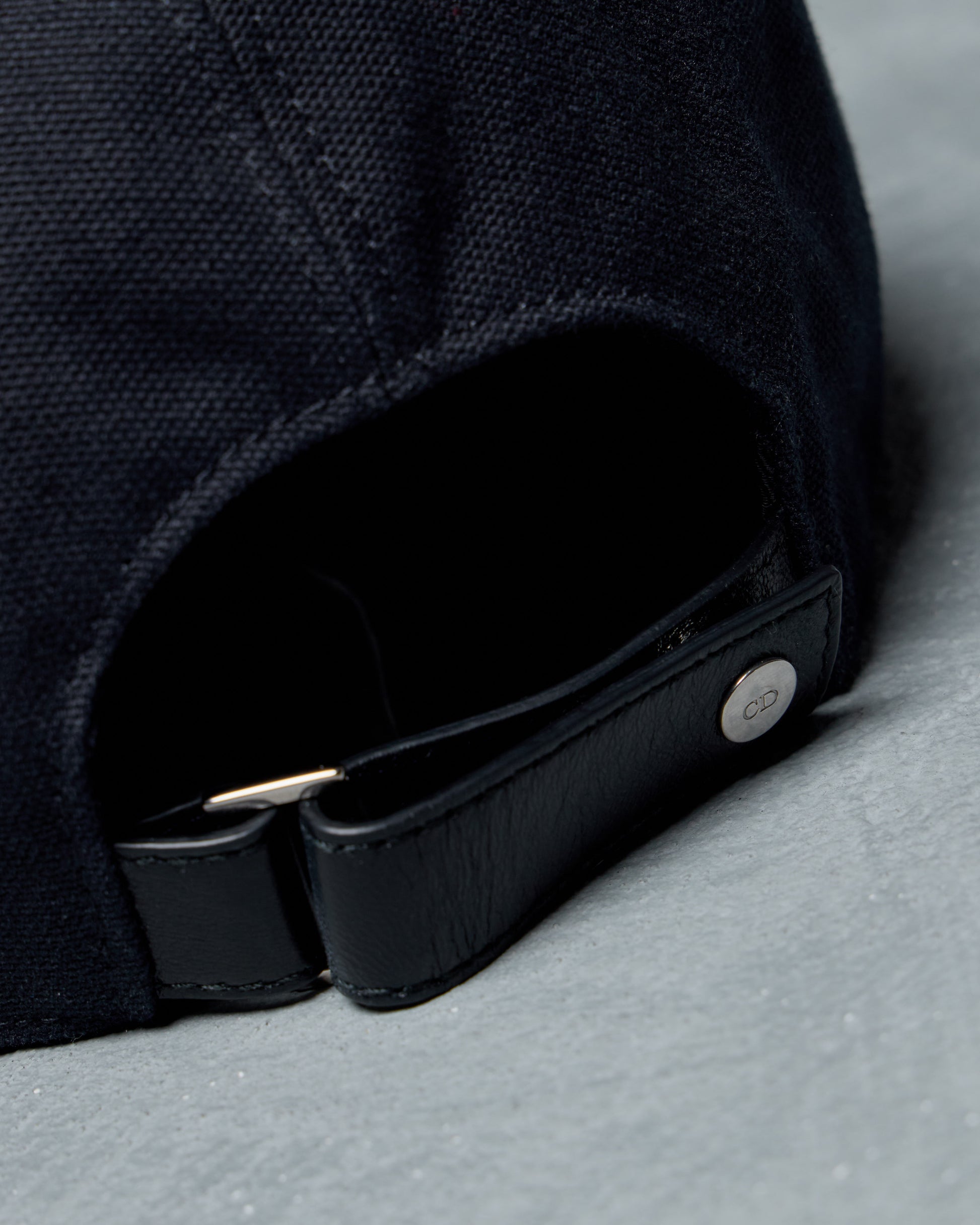 Close-up of a black Dior cap with a brand logo on a gray surface