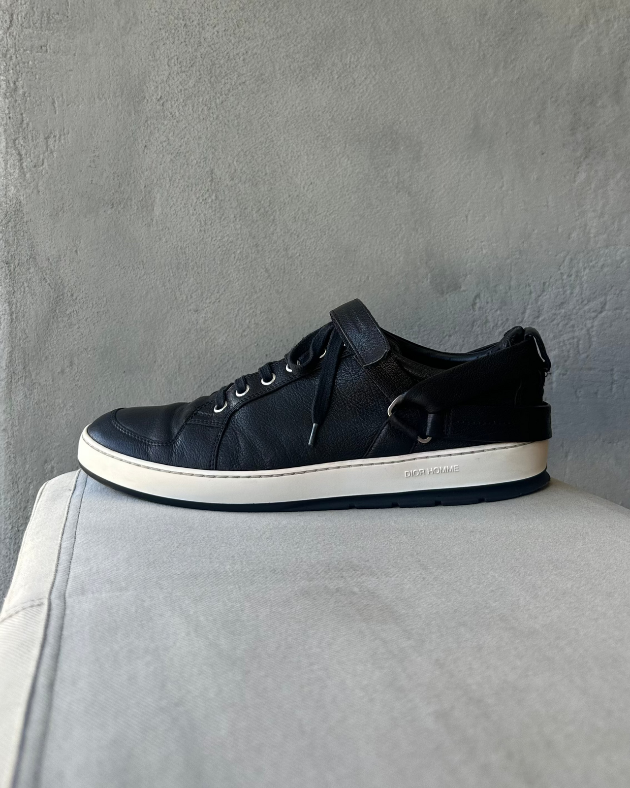 Black Dior Homme sneaker on a gray surface with a gray background