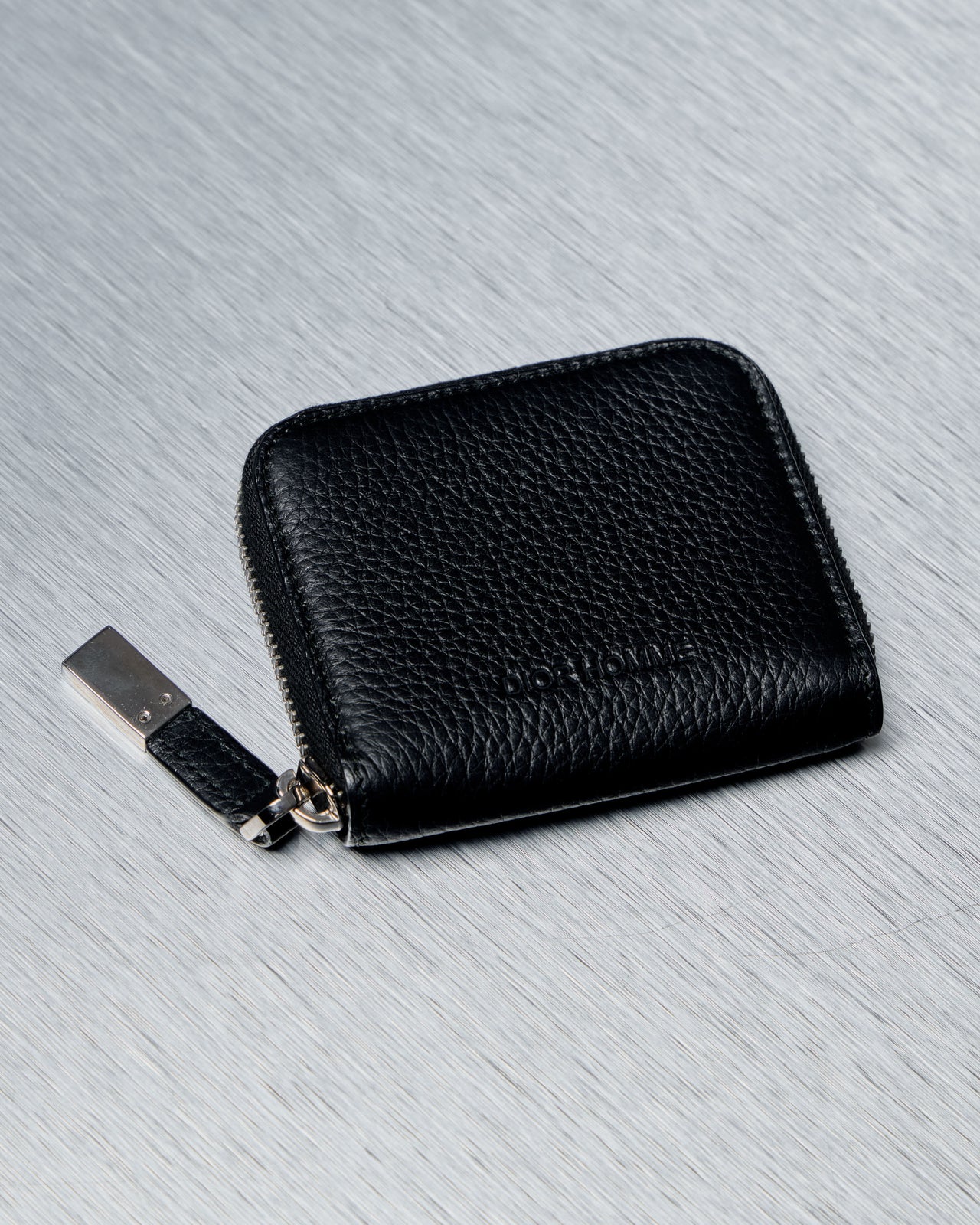 Black leather Dior Homme wallet with a zipper on a gray textured background