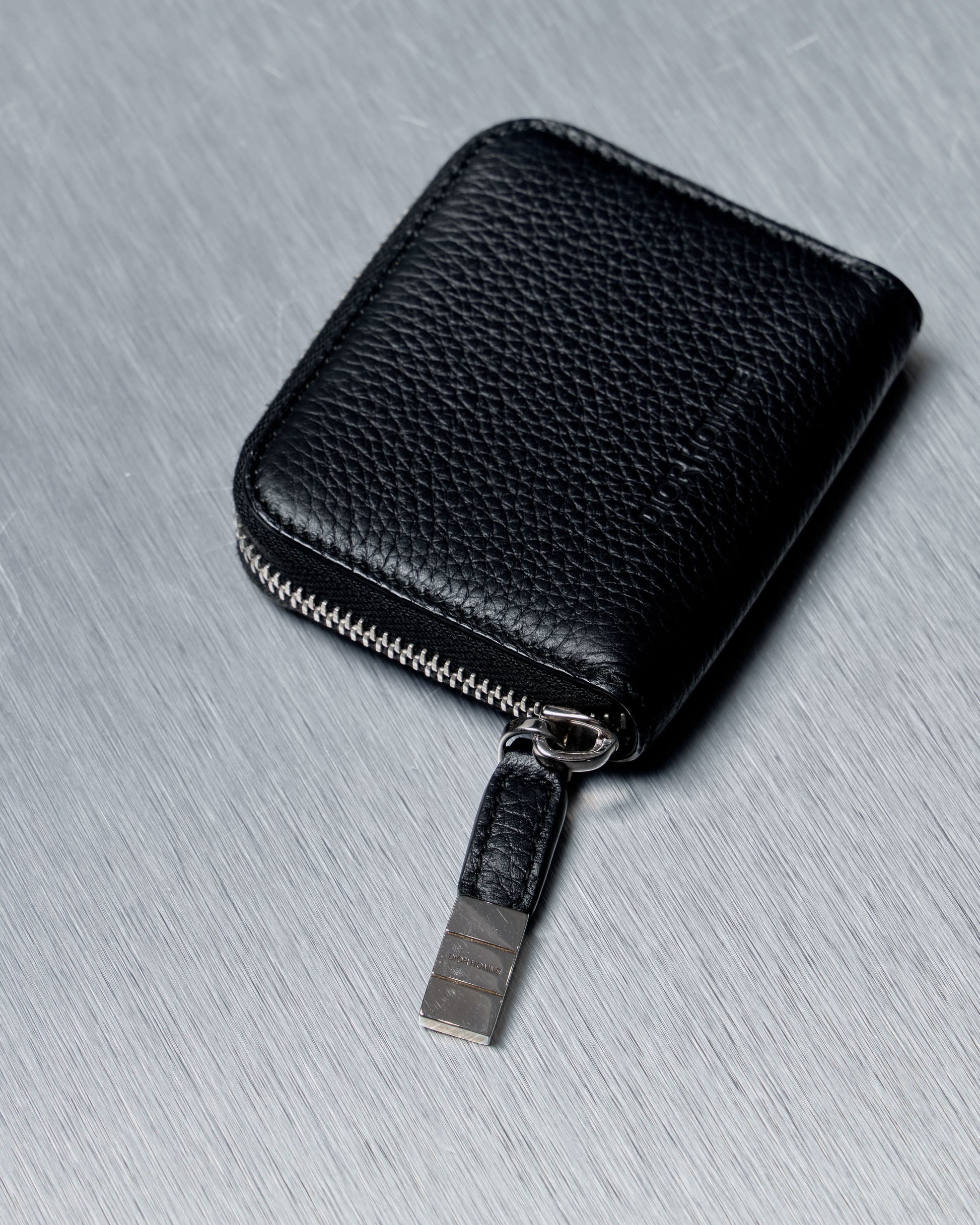 Black leather Dior Homme wallet with a keychain on a gray surface