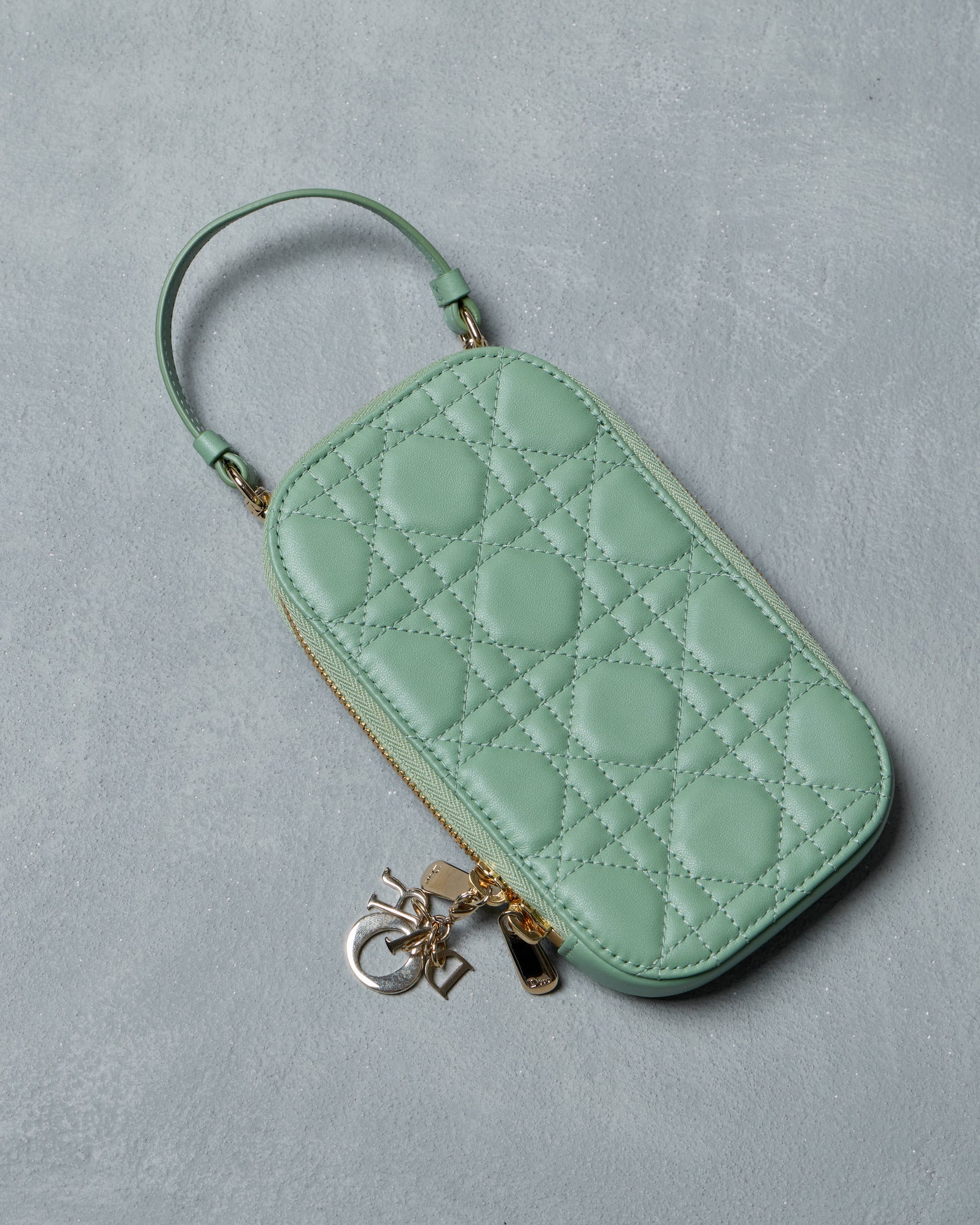 Mint green quilted Dior phone case with gold charm on a gray background
