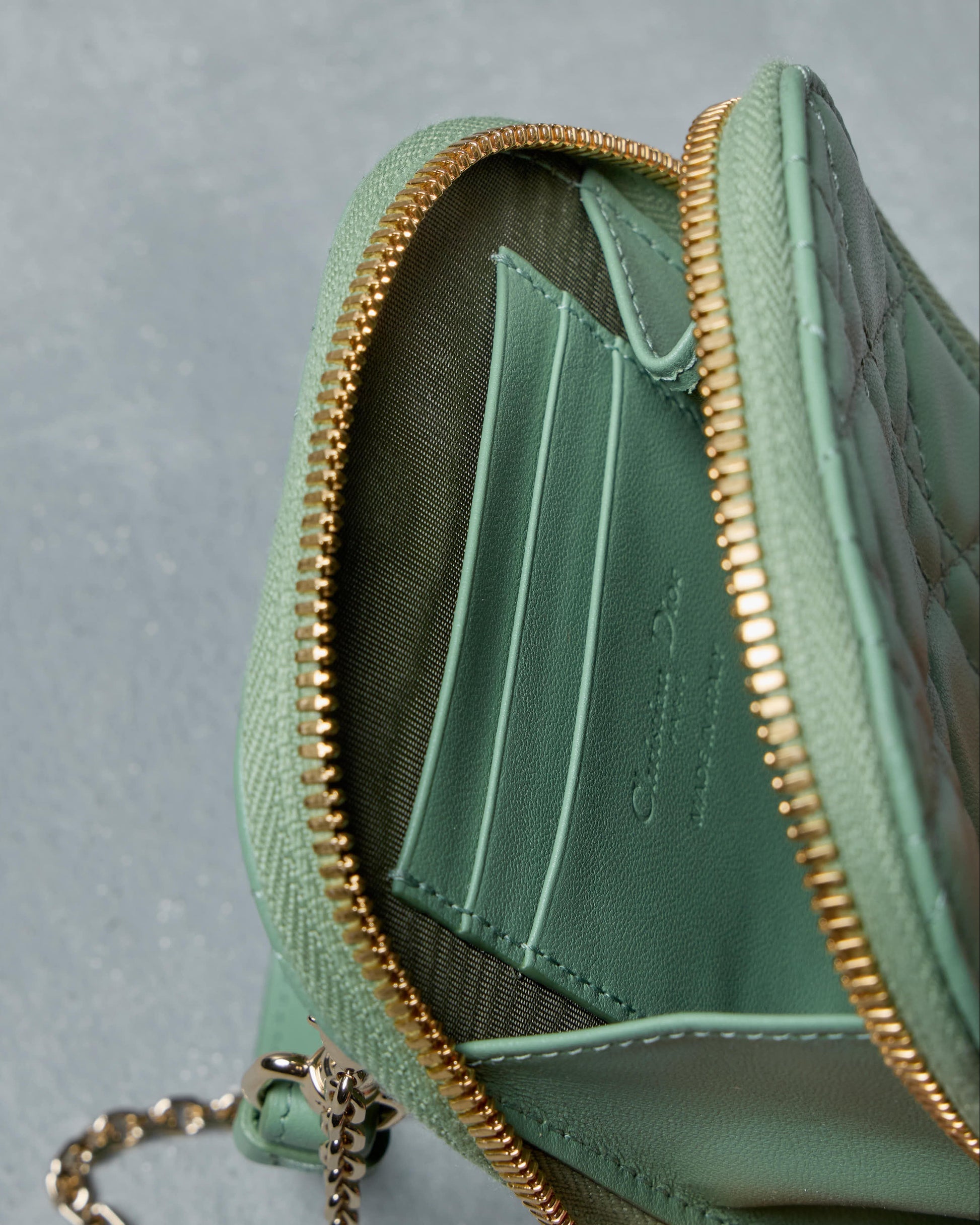 Green Dior wallet with gold zipper and chain on a gray background
