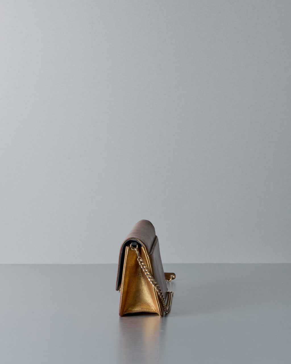 Gold Dior clutch bag on a reflective surface with a light gray background