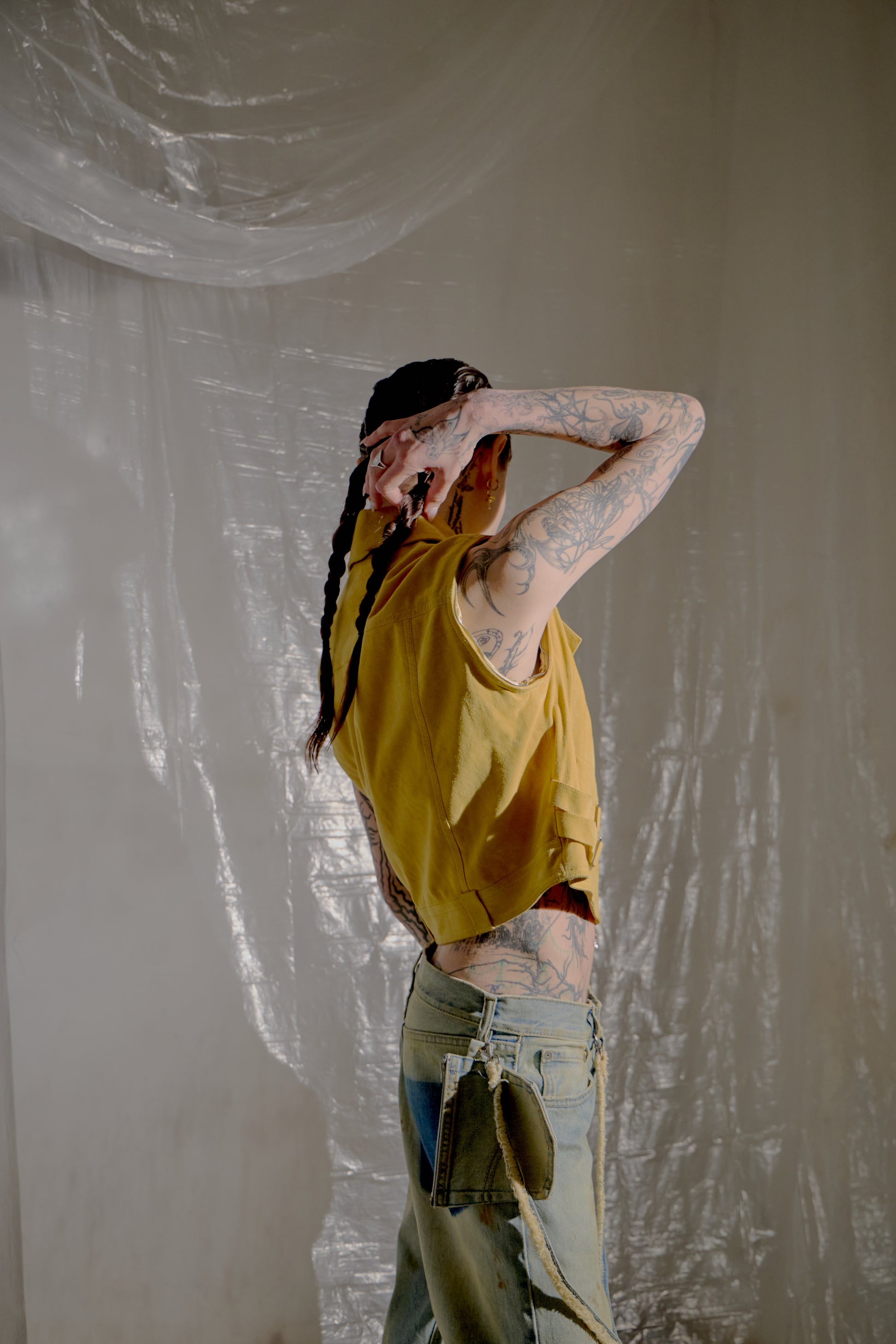 Person wearing a yellow Dior shirt and ripped jeans against a plain wall.