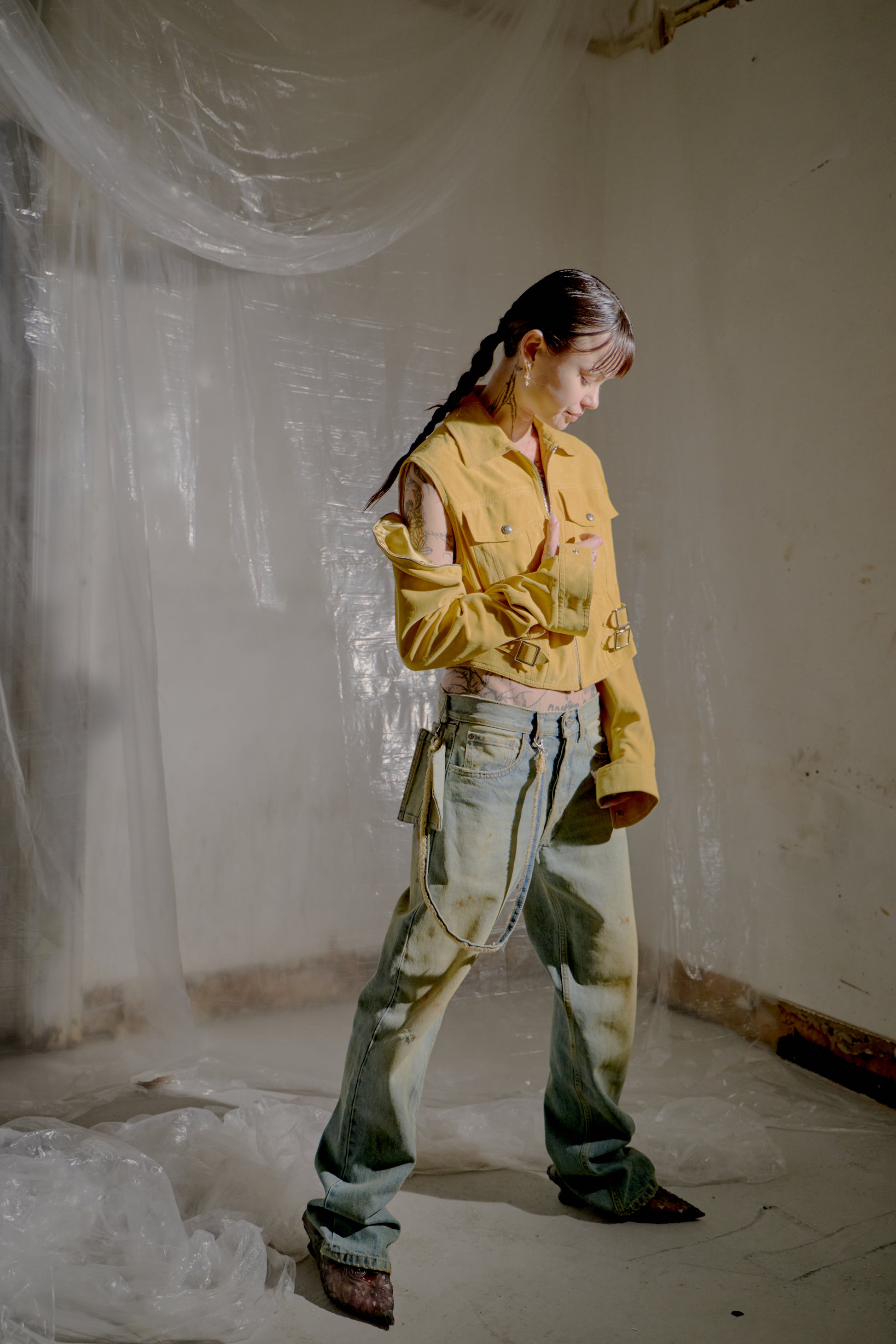 Person wearing a yellow Dior jacket and blue pants in a room with white walls and plastic sheeting.
