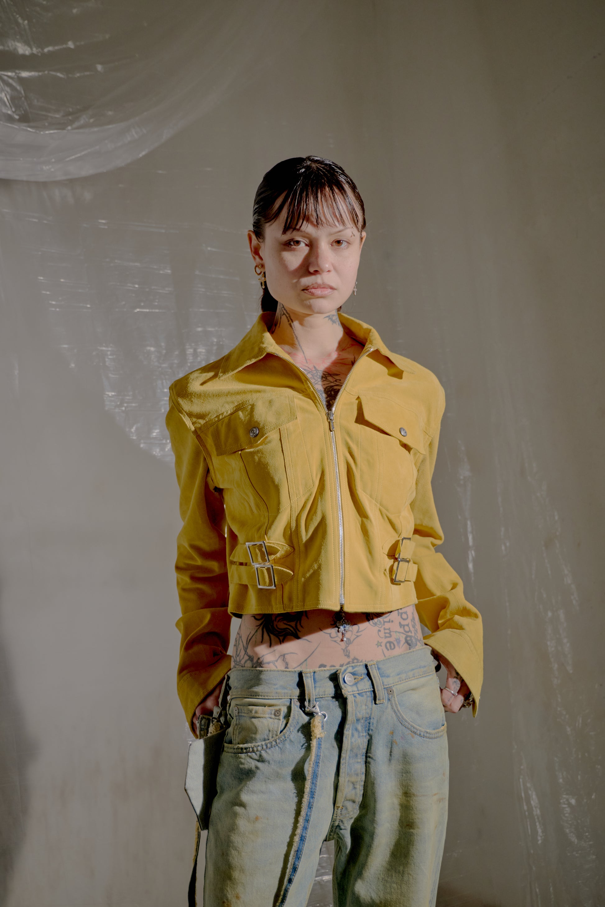 Young person in a yellow Dior jacket and jeans. The backdrop features translucent drapery.