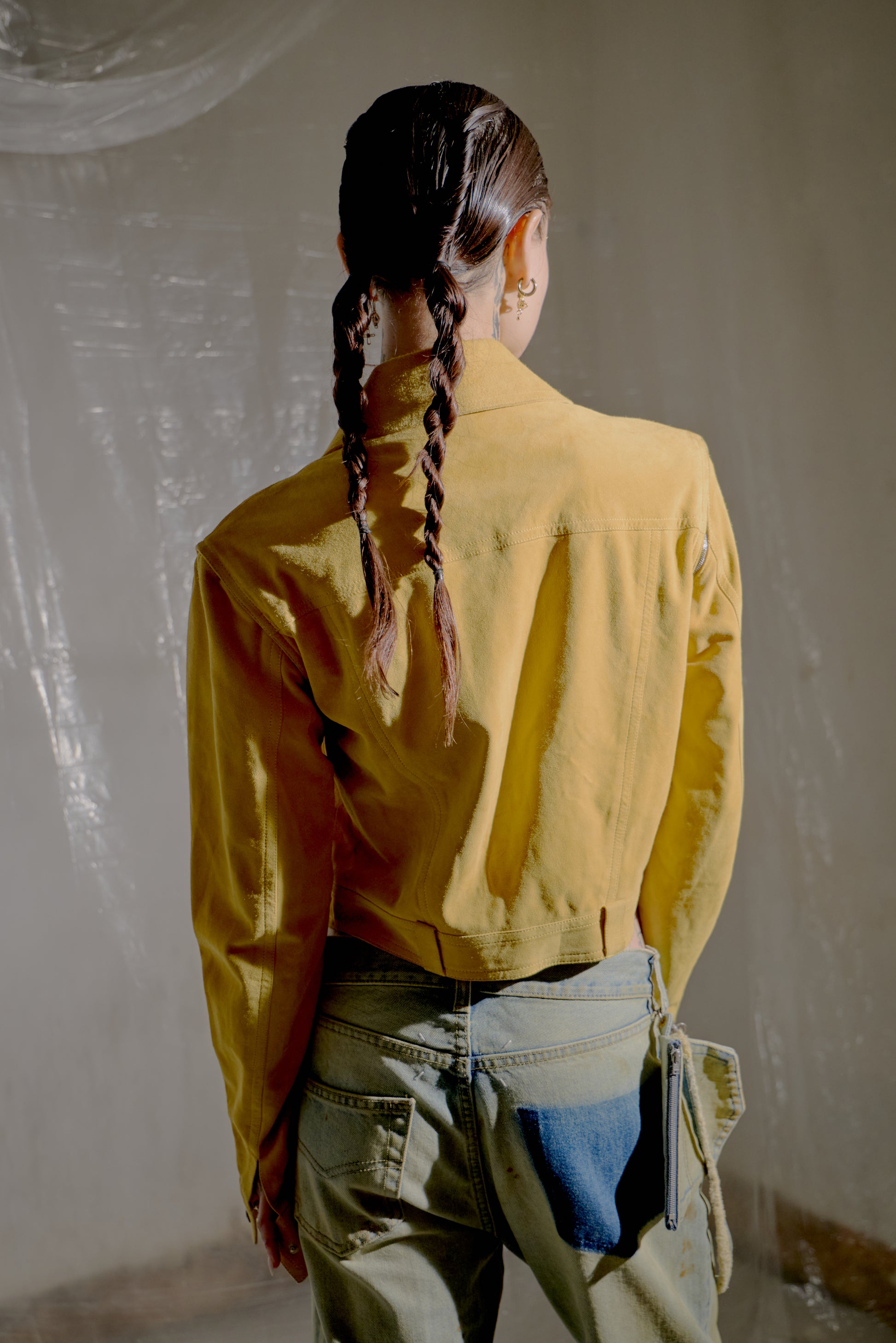 Person wearing a yellow Dior jacket and blue jeans standing in a room under construction.
