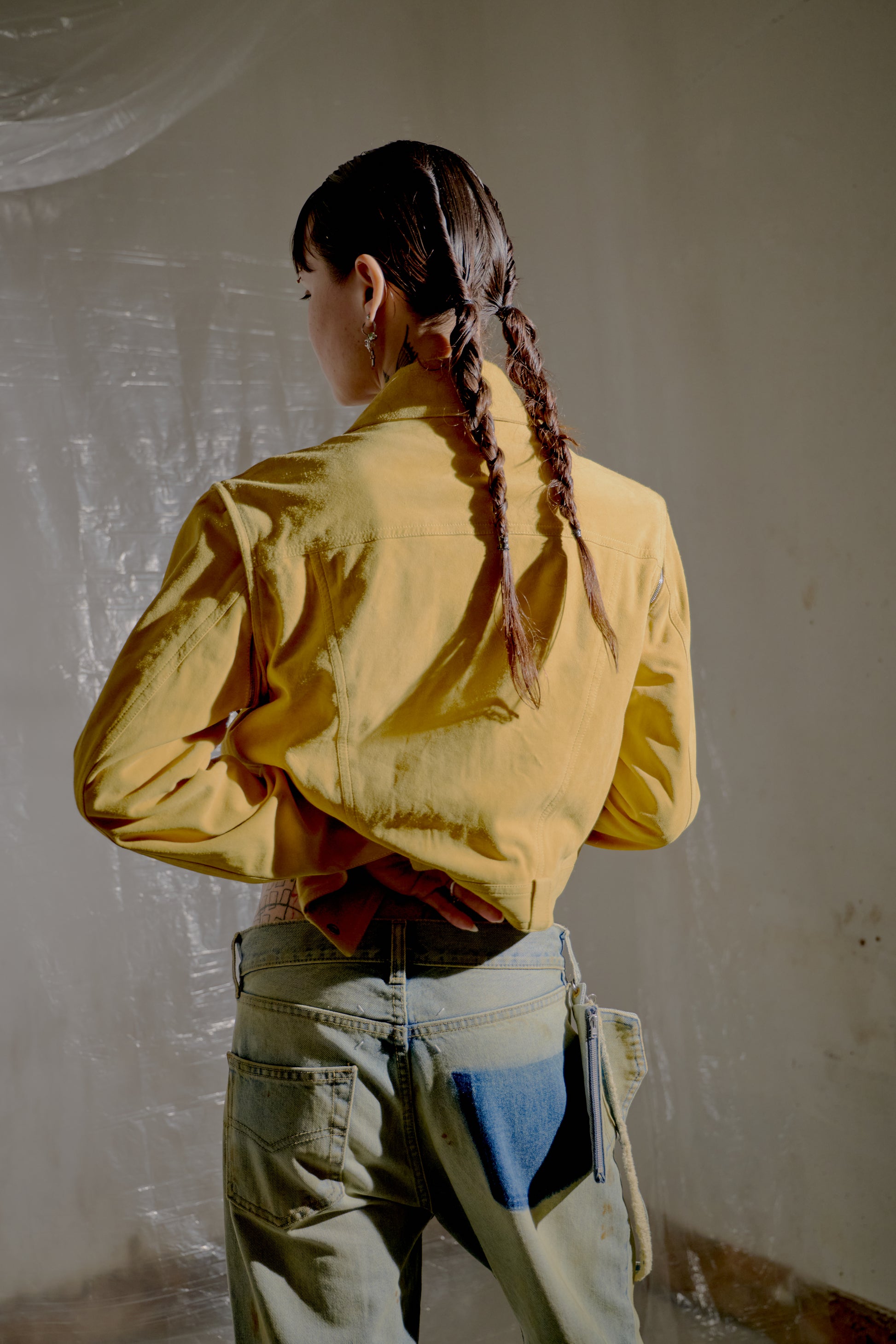 Person wearing a yellow Dior shirt and blue jeans, standing in a room with white walls.