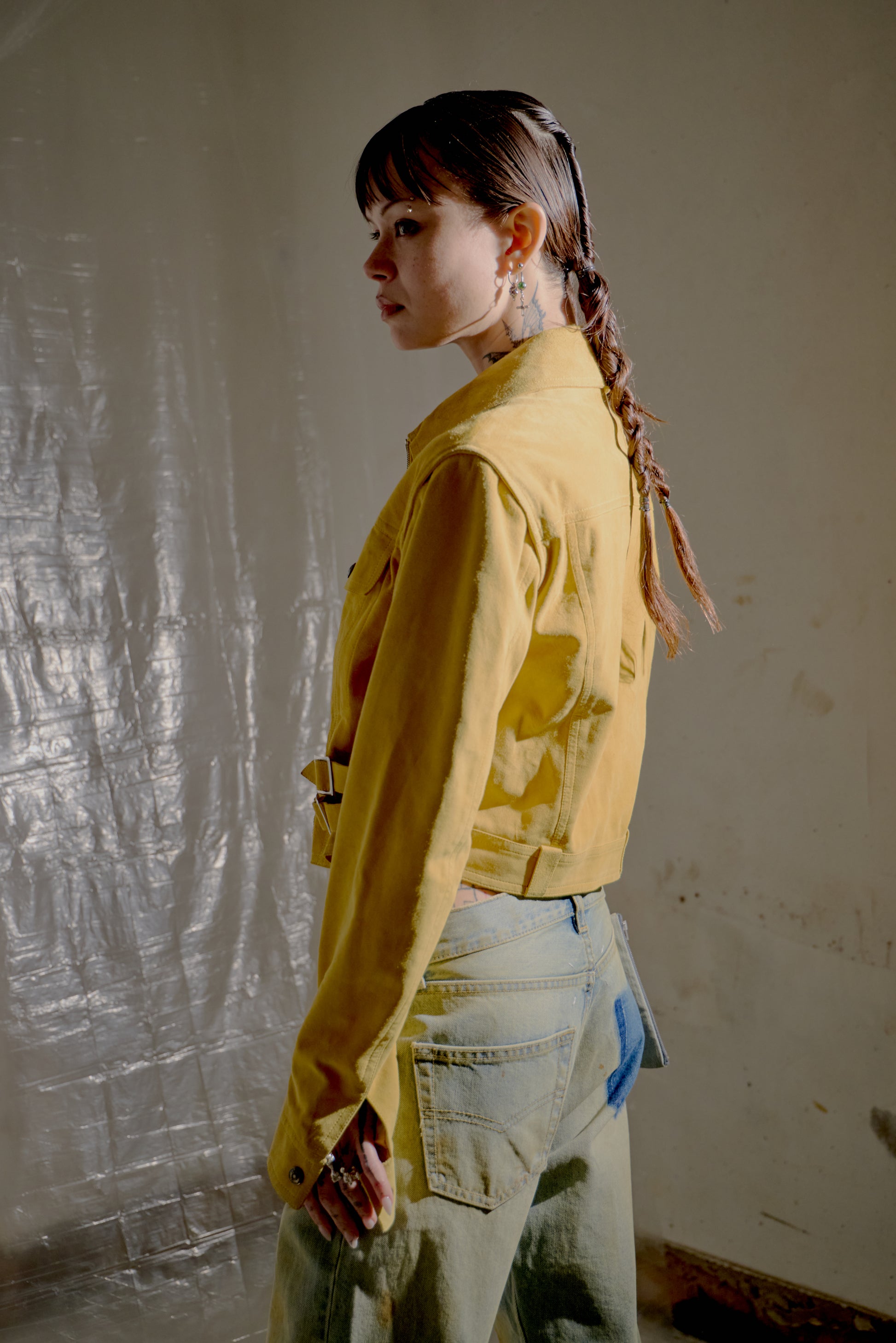 Person wearing a yellow Dior jacket and light-coloured pants against a textured wall.