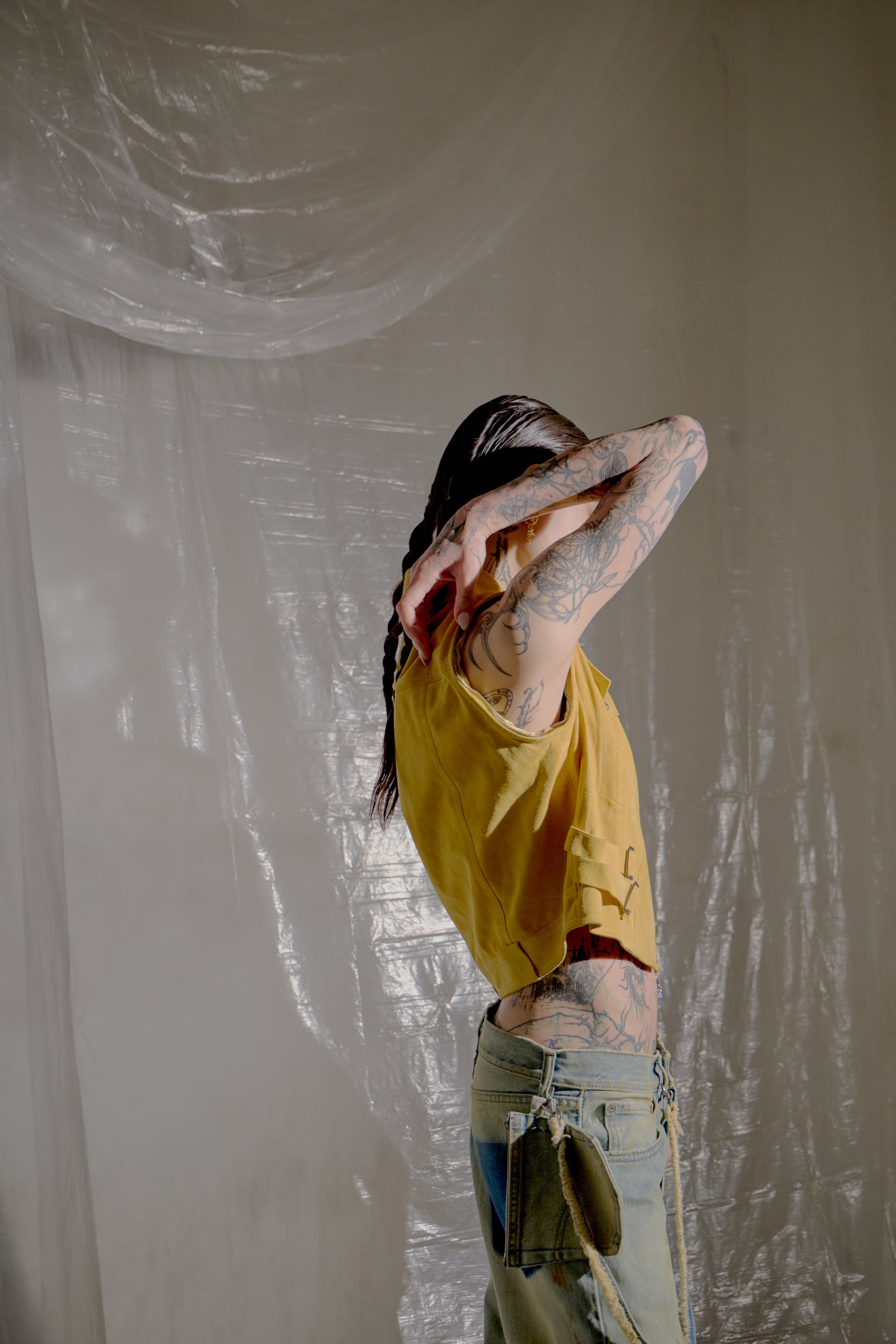 Person in a yellow Dior shirt and denim shorts standing against a white wall with plastic sheeting.