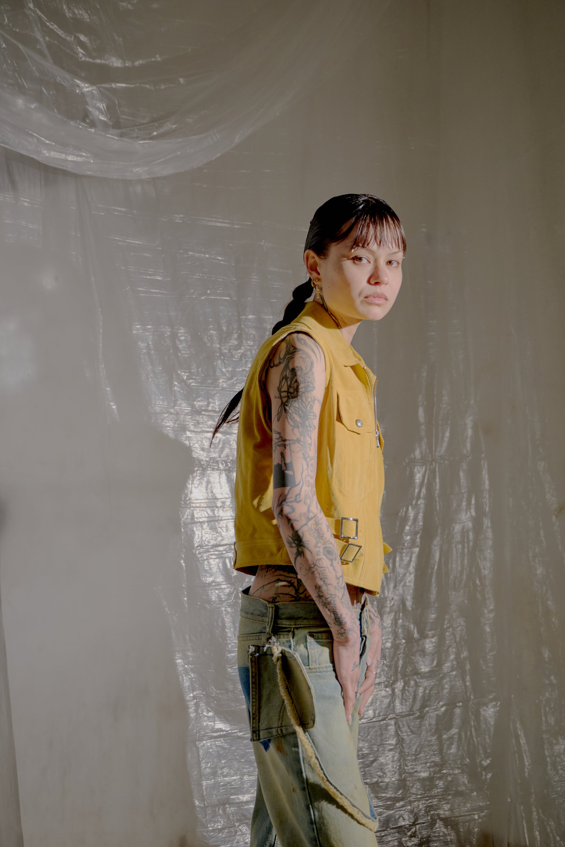 Person wearing a yellow Dior vest and blue pants against a textured white wall.