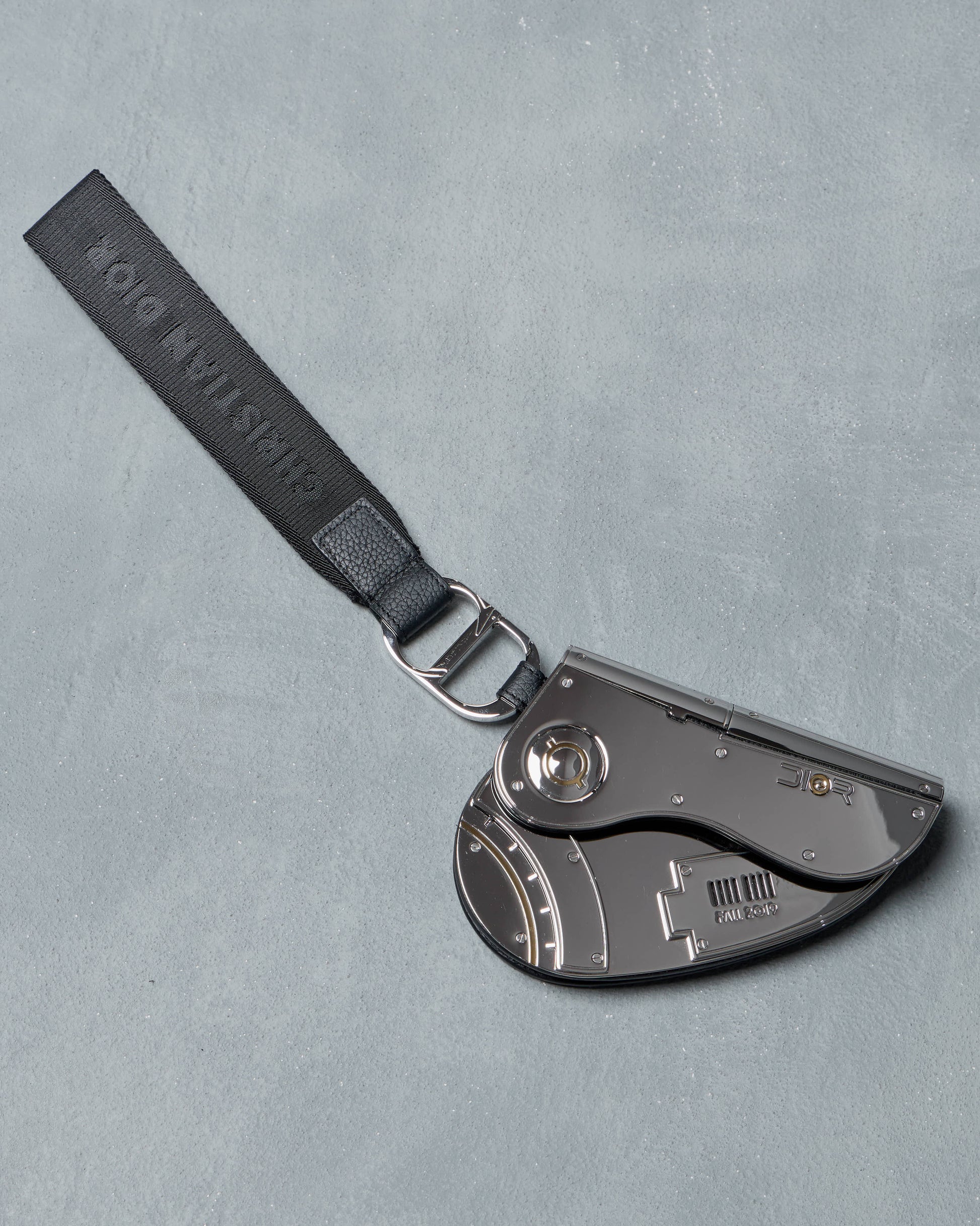 Metallic Dior x Sorayama clutch saddle bag with a strap on a gray background