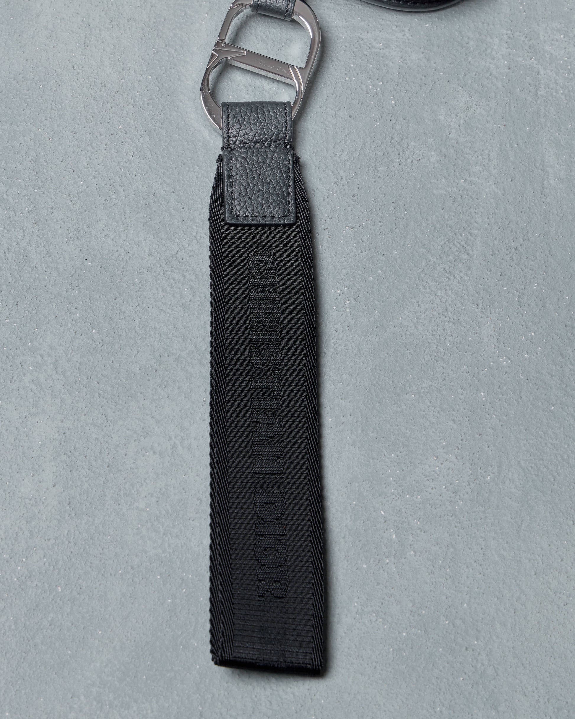 Black Dior clutch strap with metal clip on a gray background