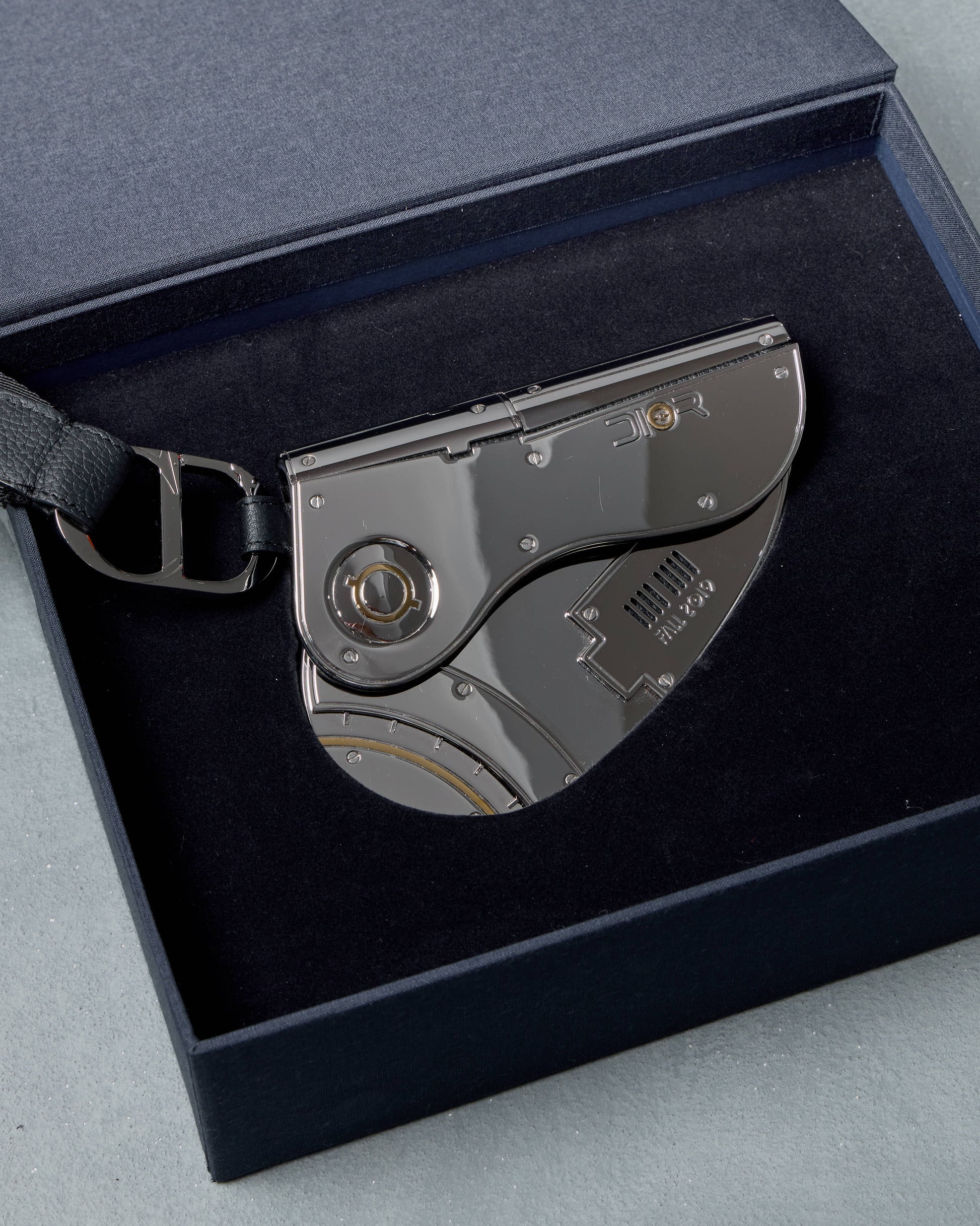 Silver Dior clutch with a black sheath in a dark blue box on a gray surface
