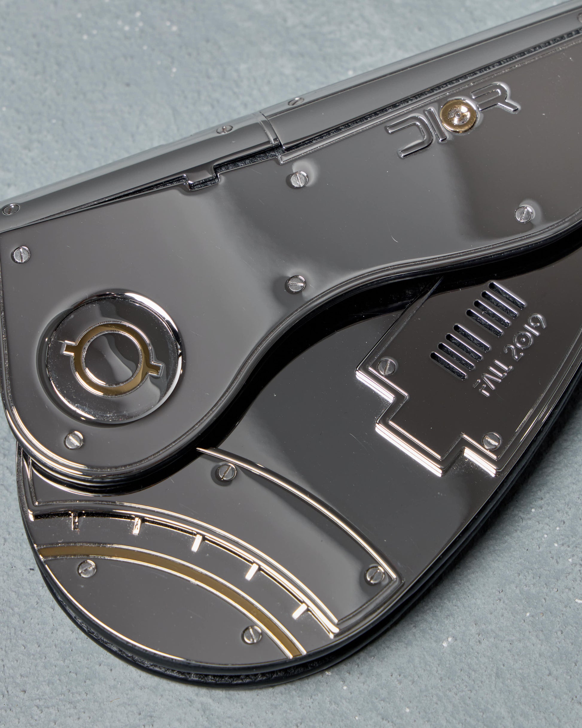 Close-up of a silver Dior mini saddle bag with visible branding on a gray background